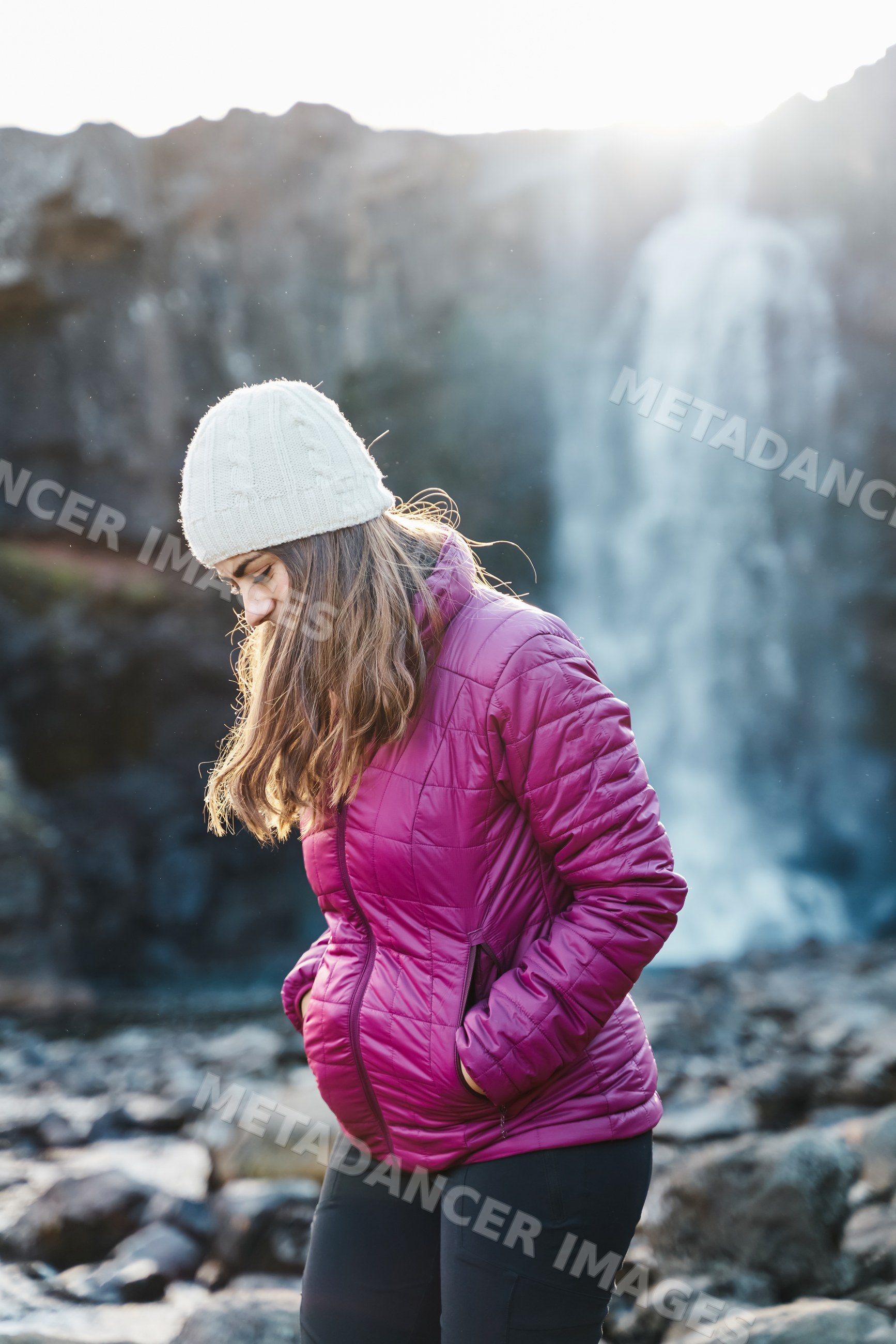 A white woman walks near a waterfall in Iceland wearing winter