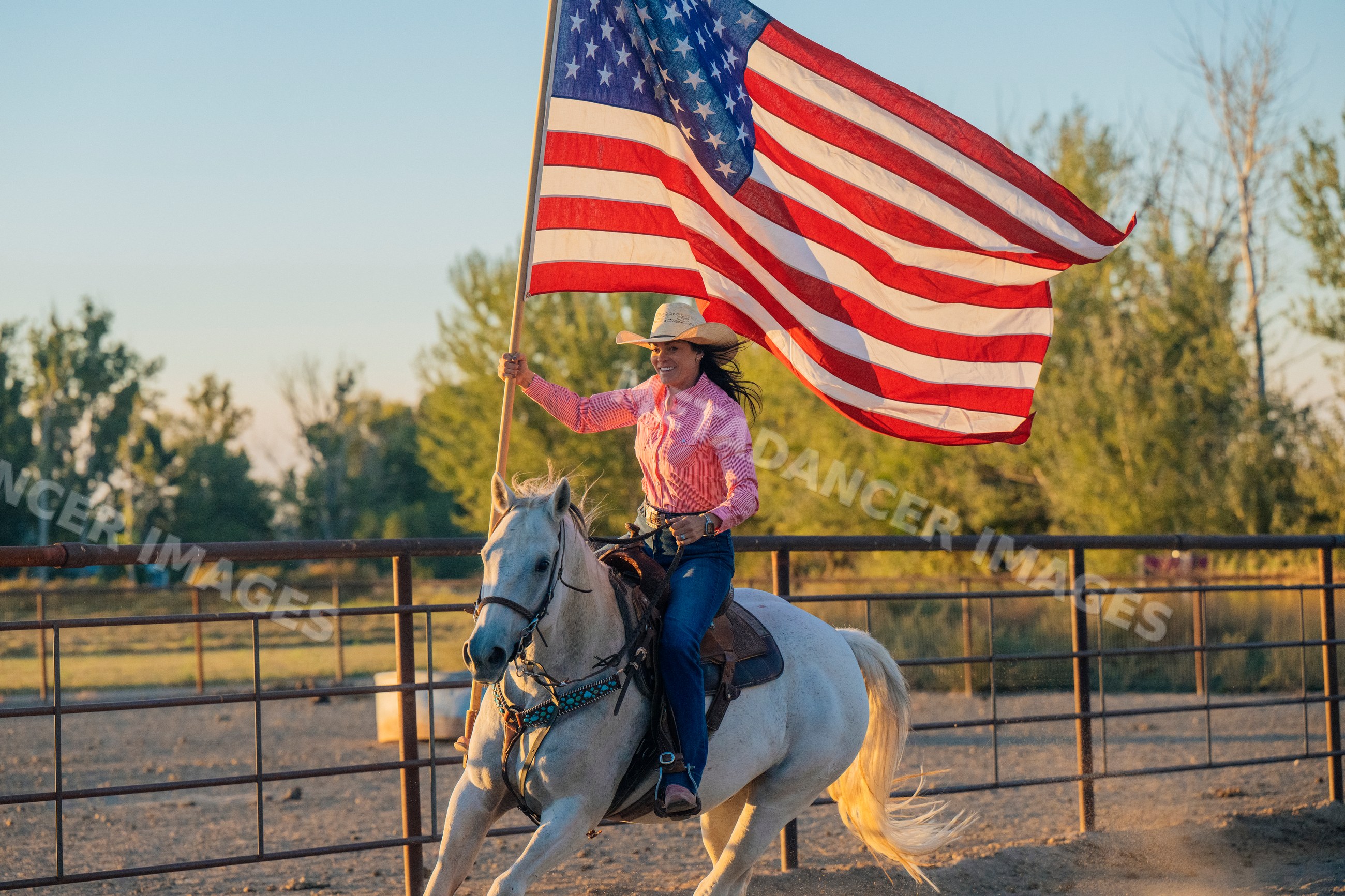 Woman riding a white horse holding an american flag at a ranch