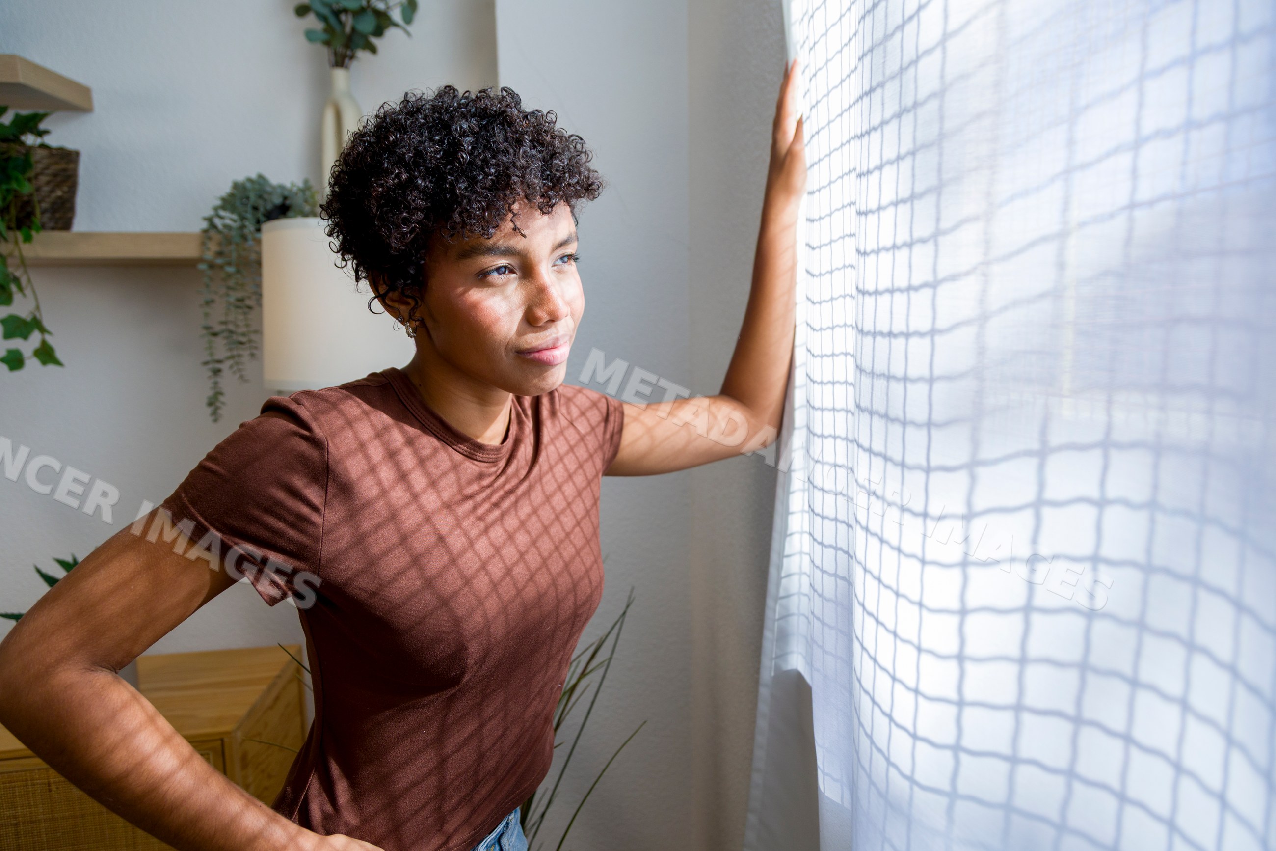 Young African American woman standing by window curtain inside home