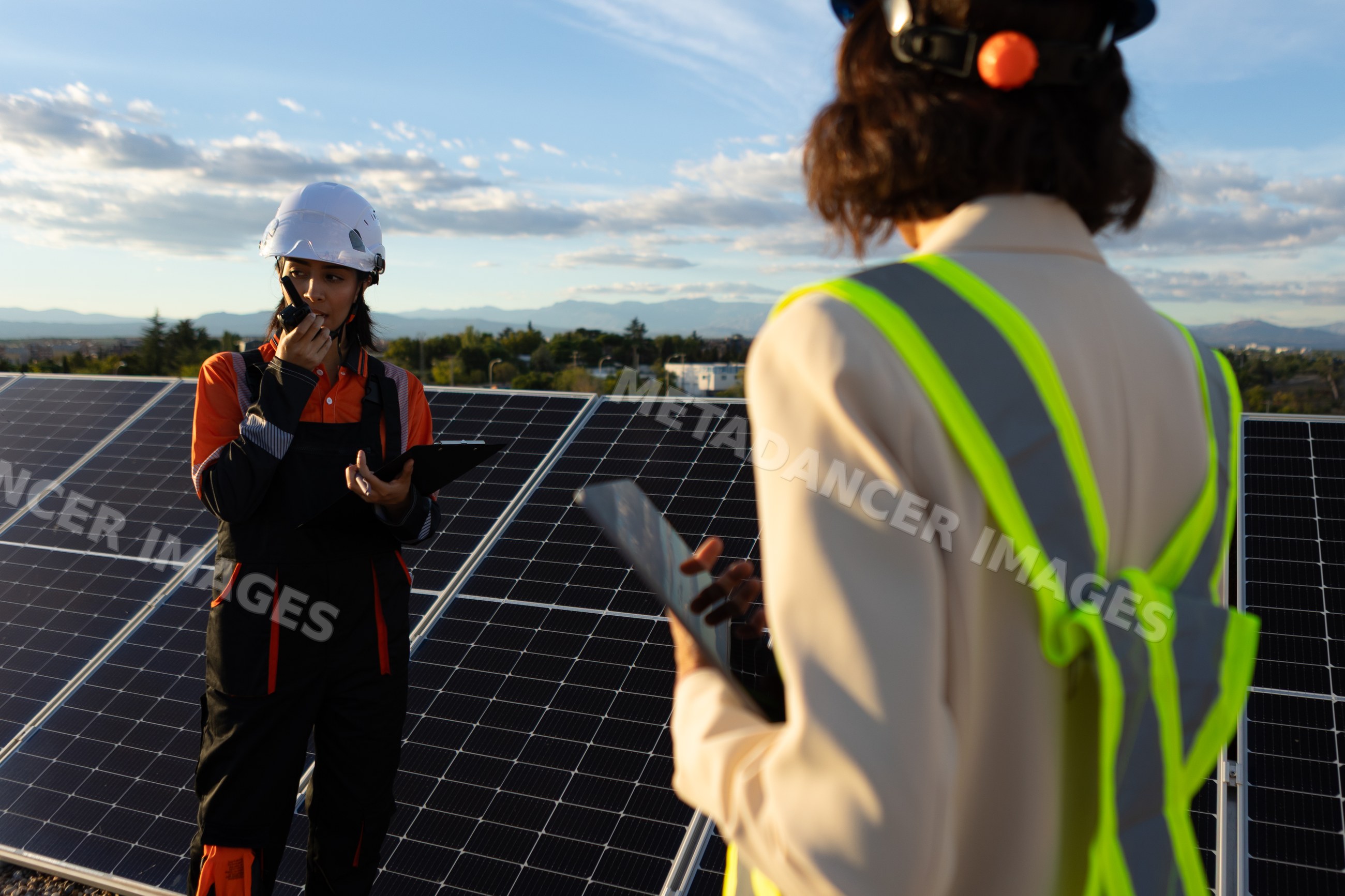 Hispanic and white worker inspecting solar panels and communicating