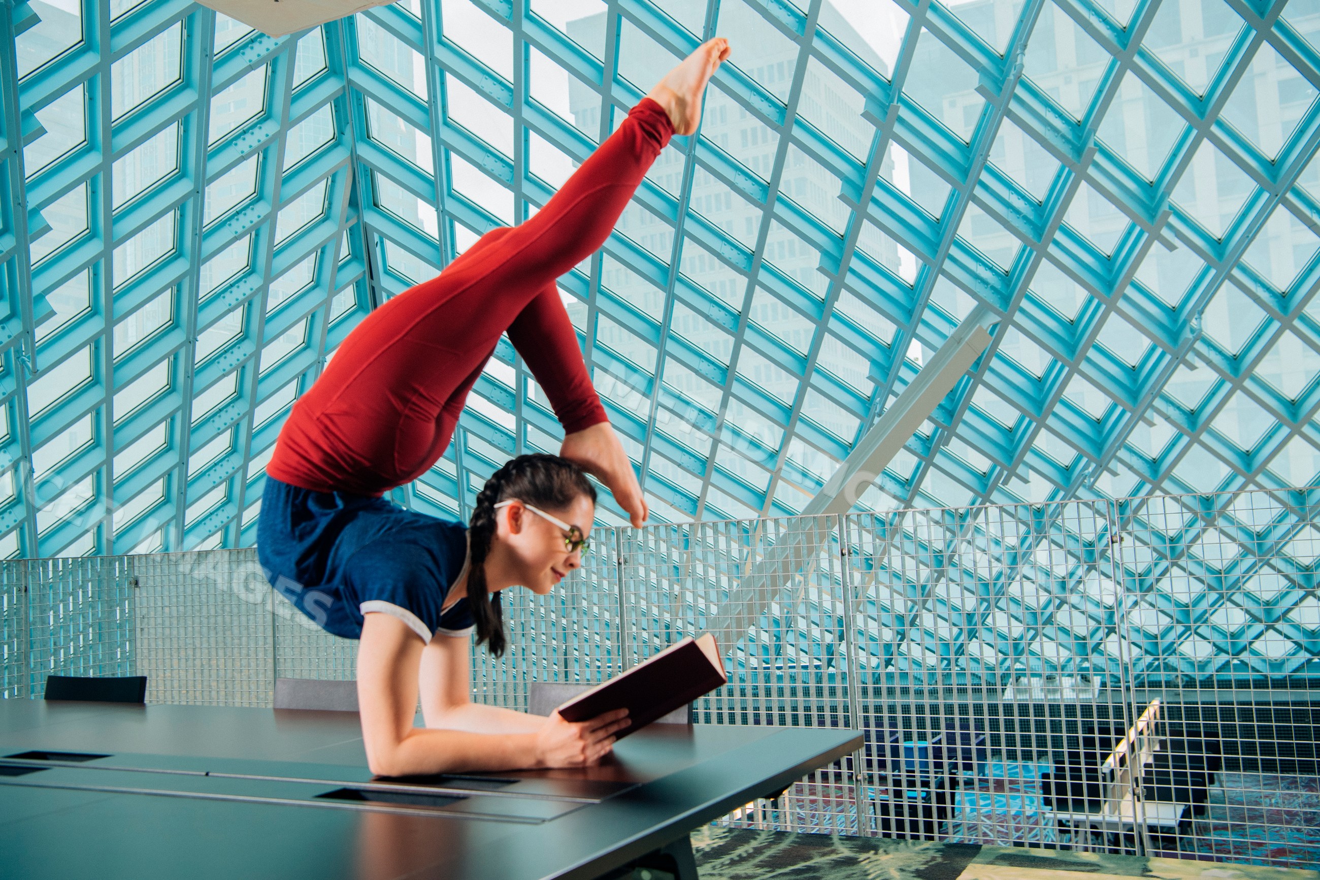 A flexible young woman reads a book balancing on a table
