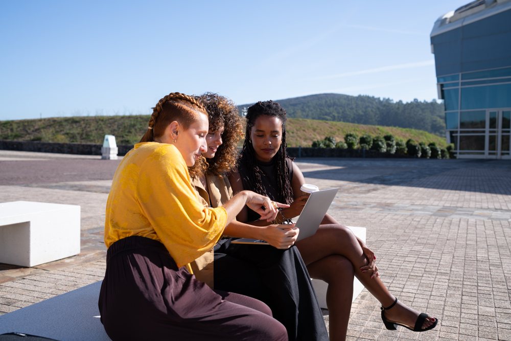 Three African American and white women discussing with tablet outdoors