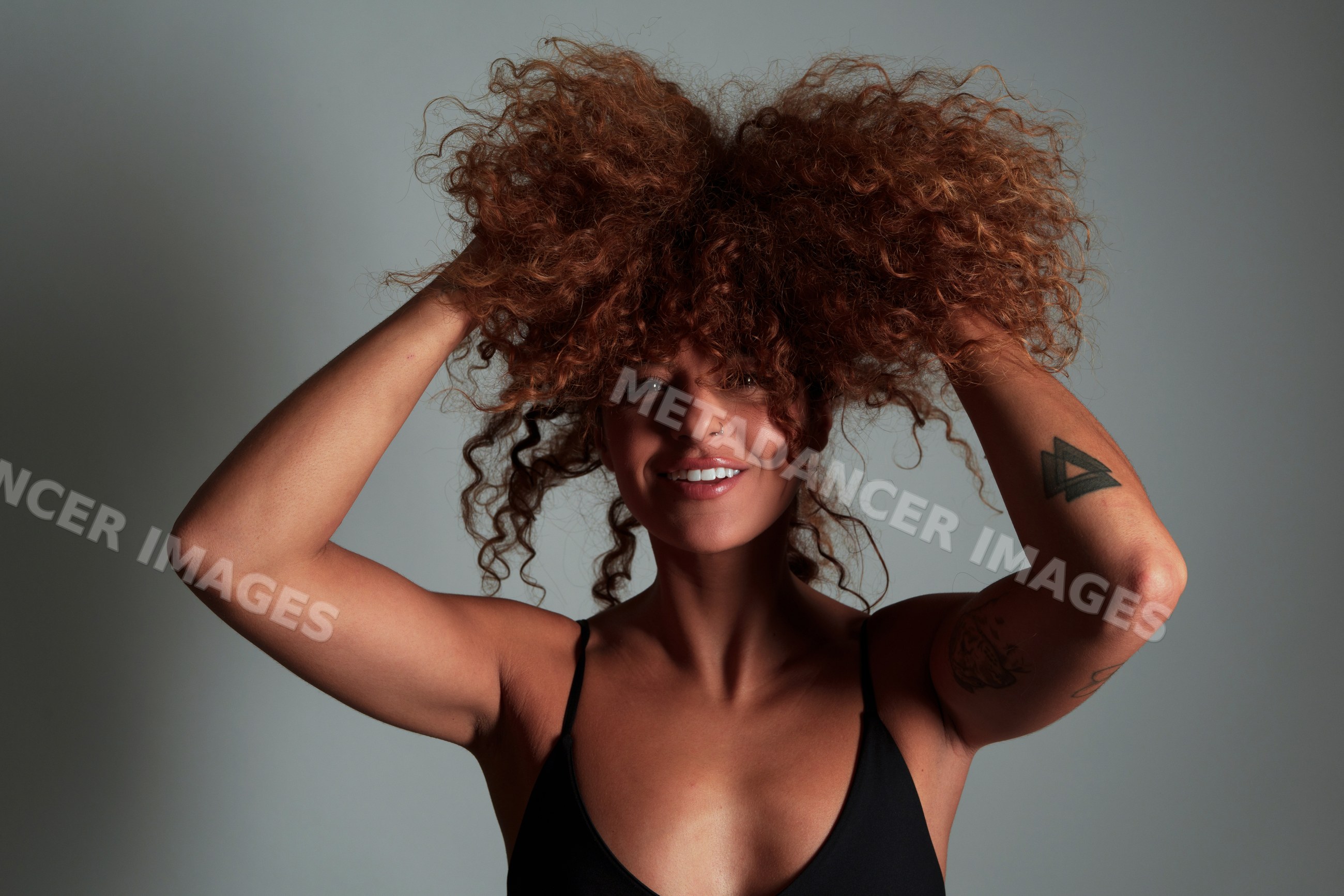 Hispanic woman with curly reddish hair and tattoos posing
