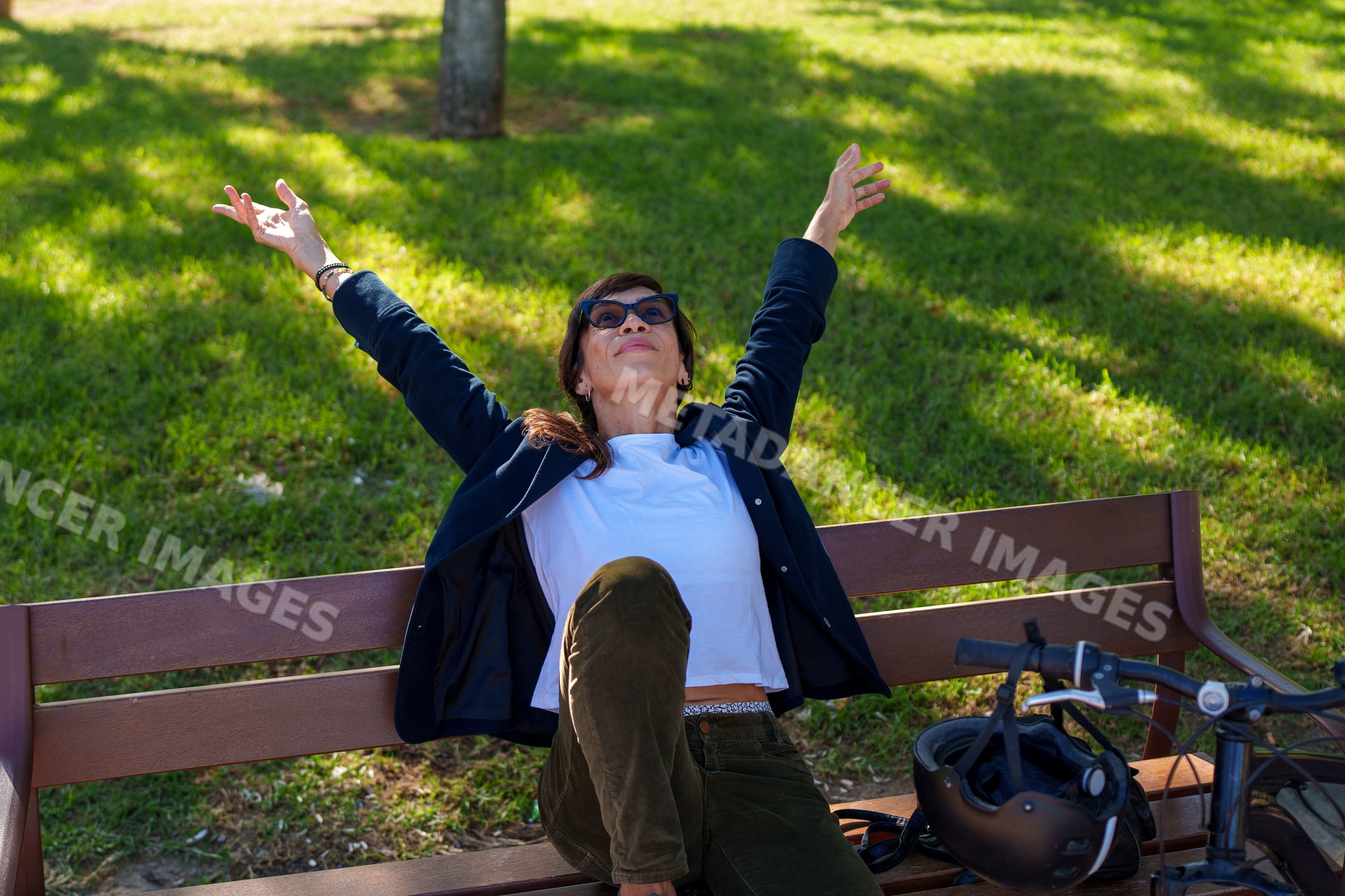 Hispanic woman sitting on bench stretching outdoors next to bicycle