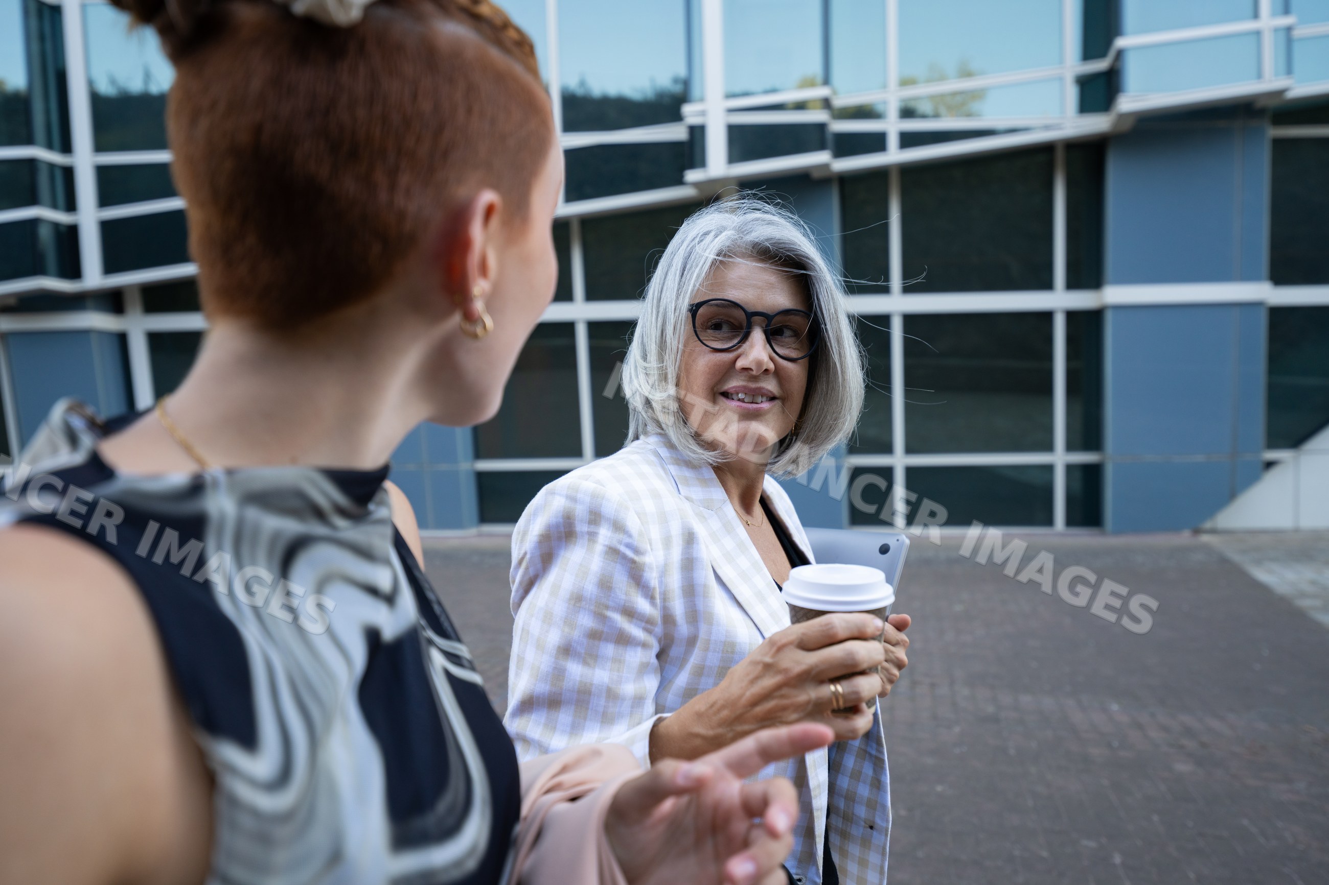 Two businesswomen conversing outside office building with coffee