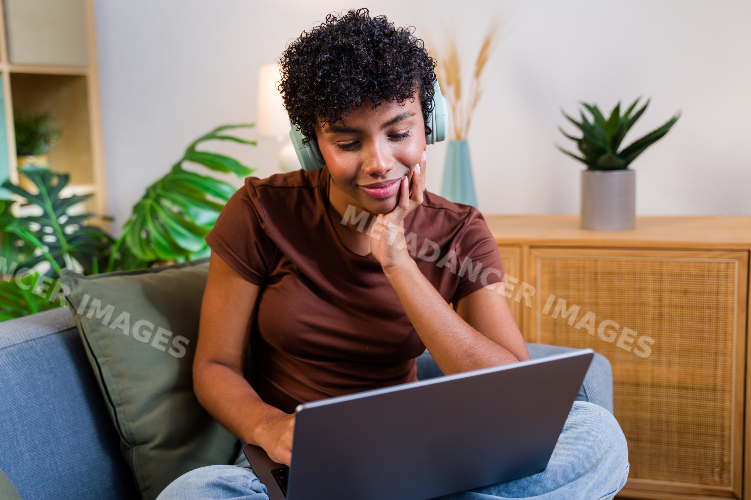 African American woman using laptop with headphones sitting on couch
