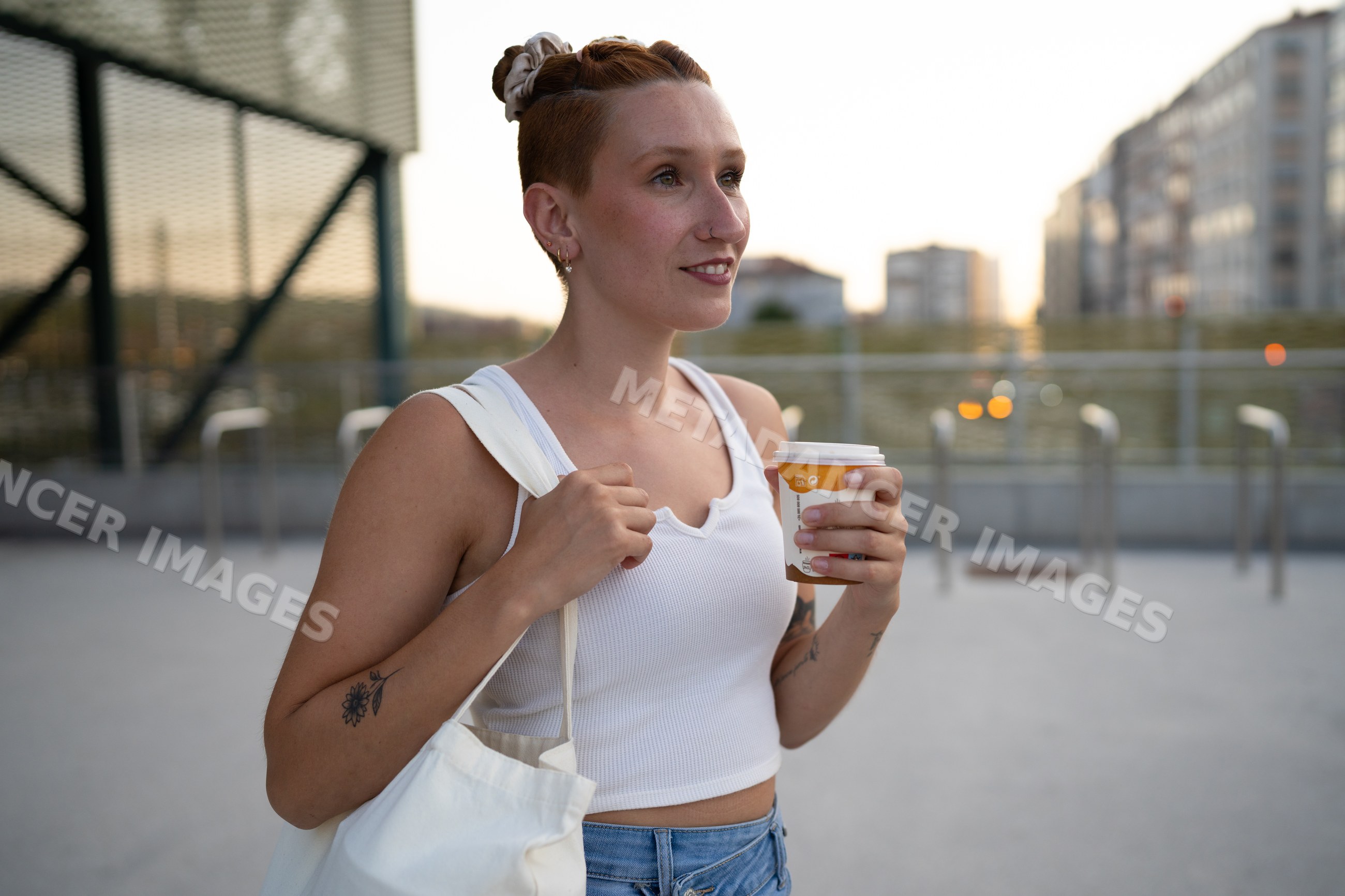 A young white woman holds coffee and carries a tote bag