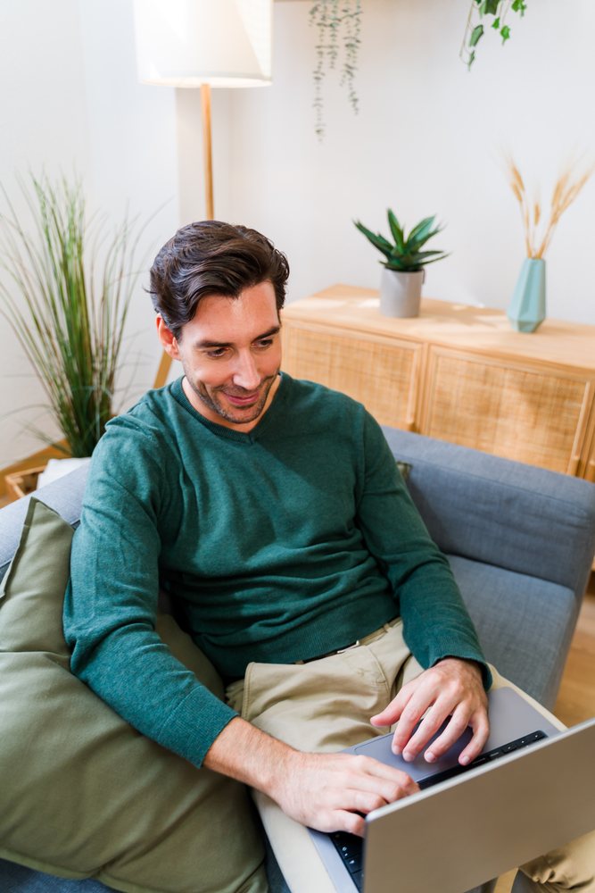 White man working on laptop sitting on sofa in modern living room