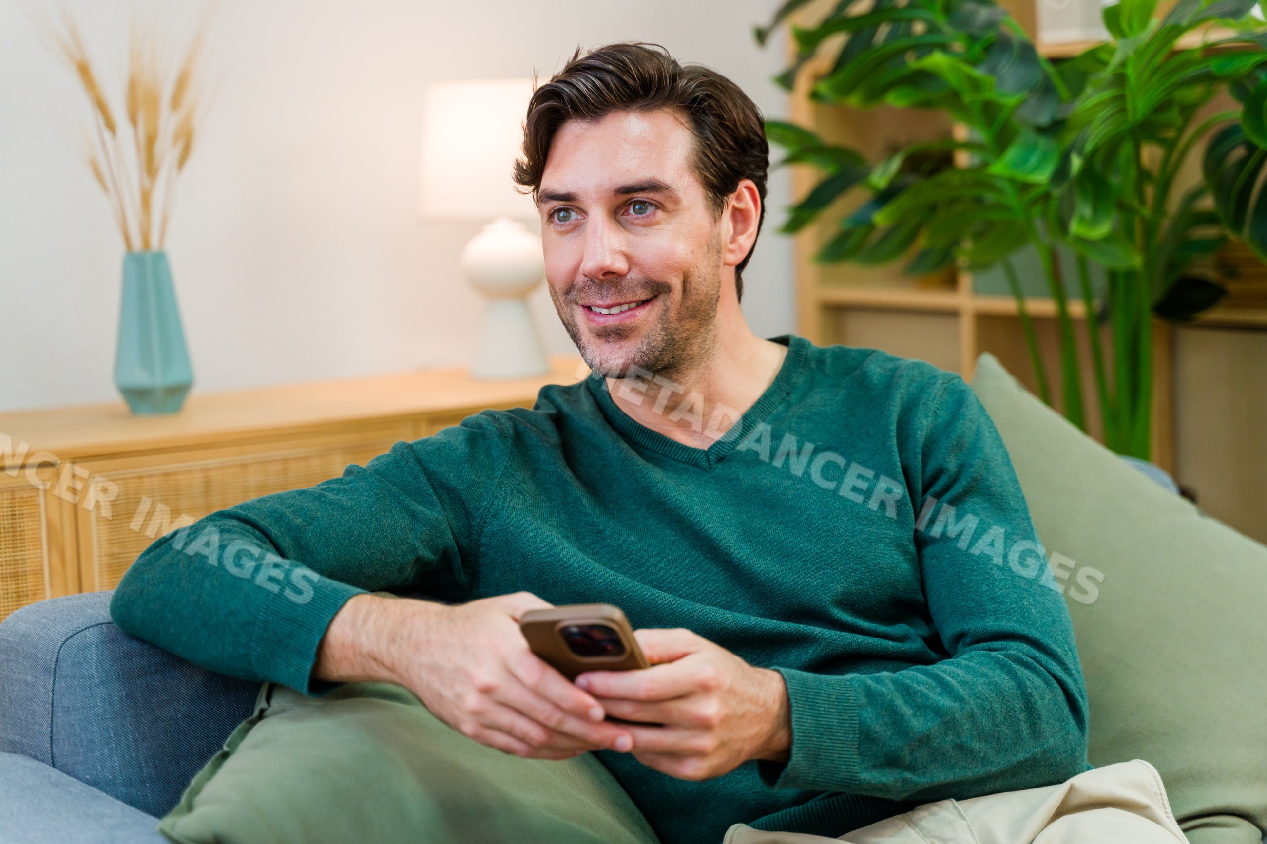 White man holding smartphone smiling indoors on couch