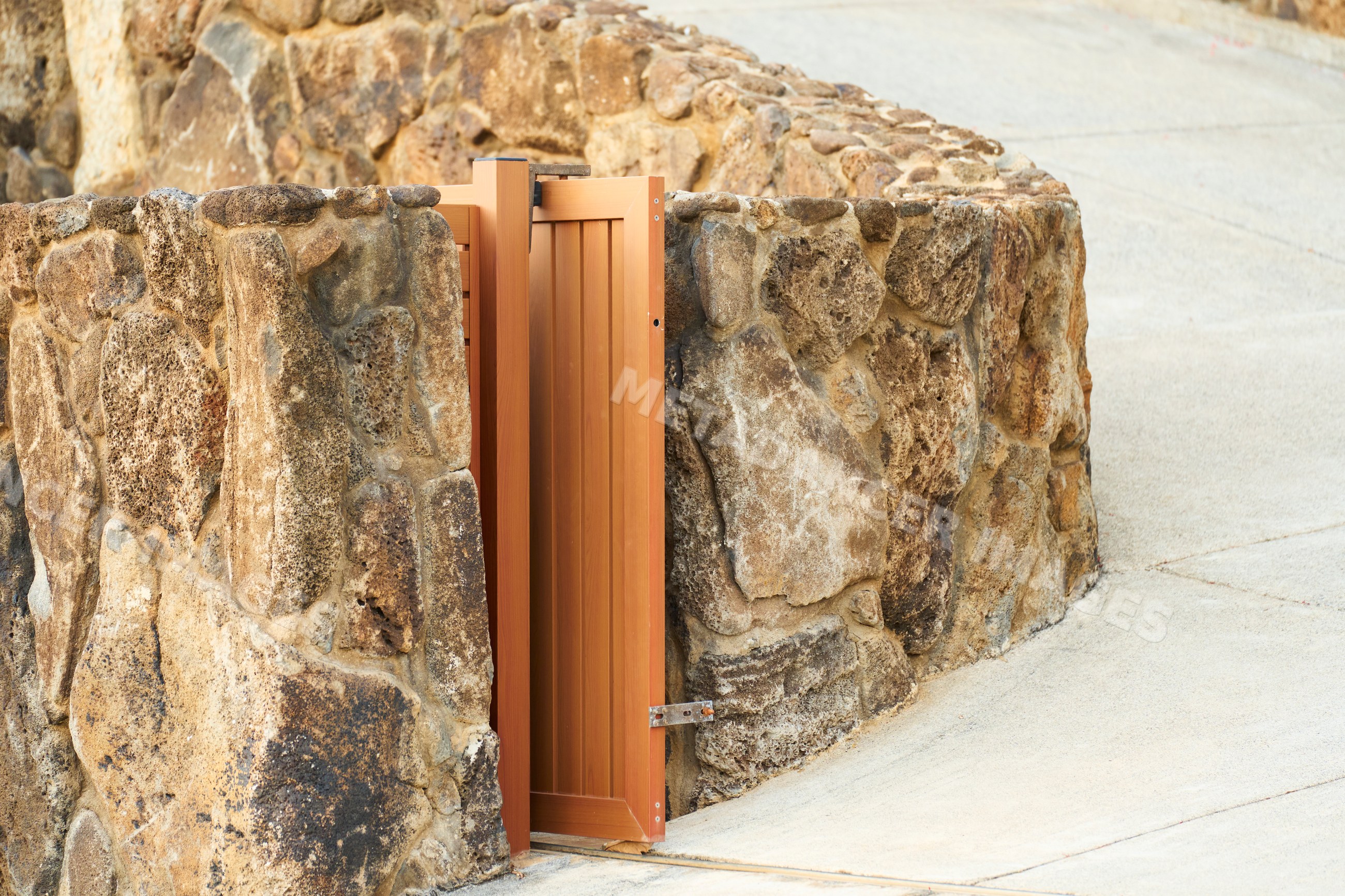 Stone wall with wooden gate along curved sidewalk