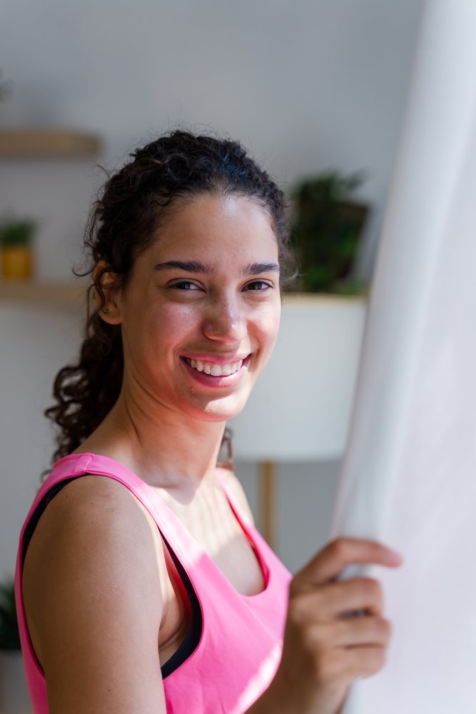 A smiling Hispanic woman holding a curtain in a bright indoor setting