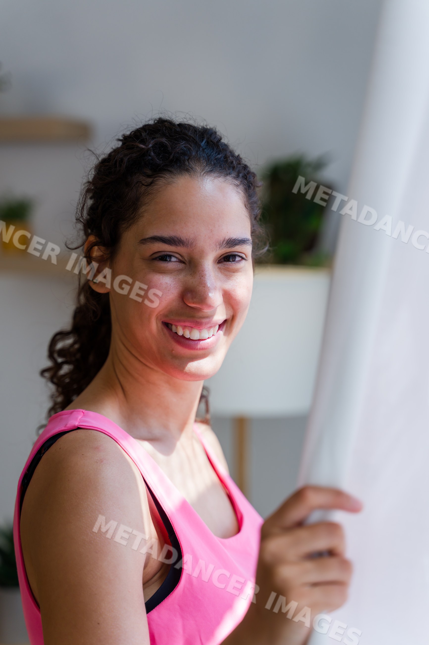 A smiling Hispanic woman holding a curtain in a bright indoor setting