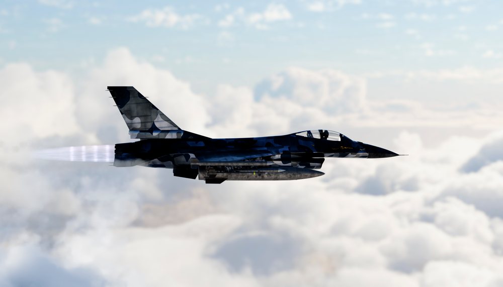Military jet flying fast above clouds in clear sky