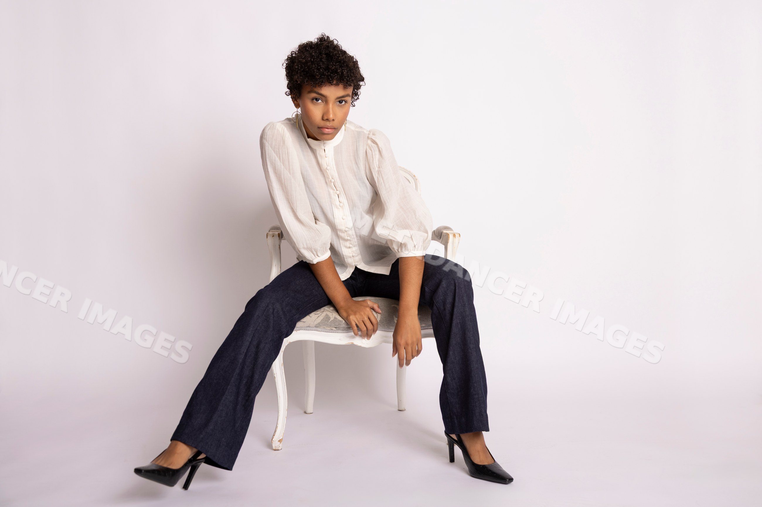 Hispanic woman sitting in chair wearing white blouse and dark pants