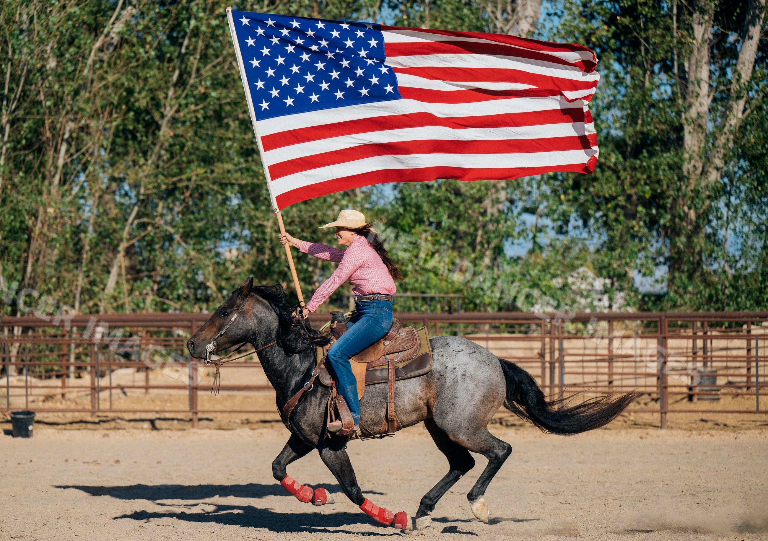 White woman riding horse carrying american flag in outdoor arena