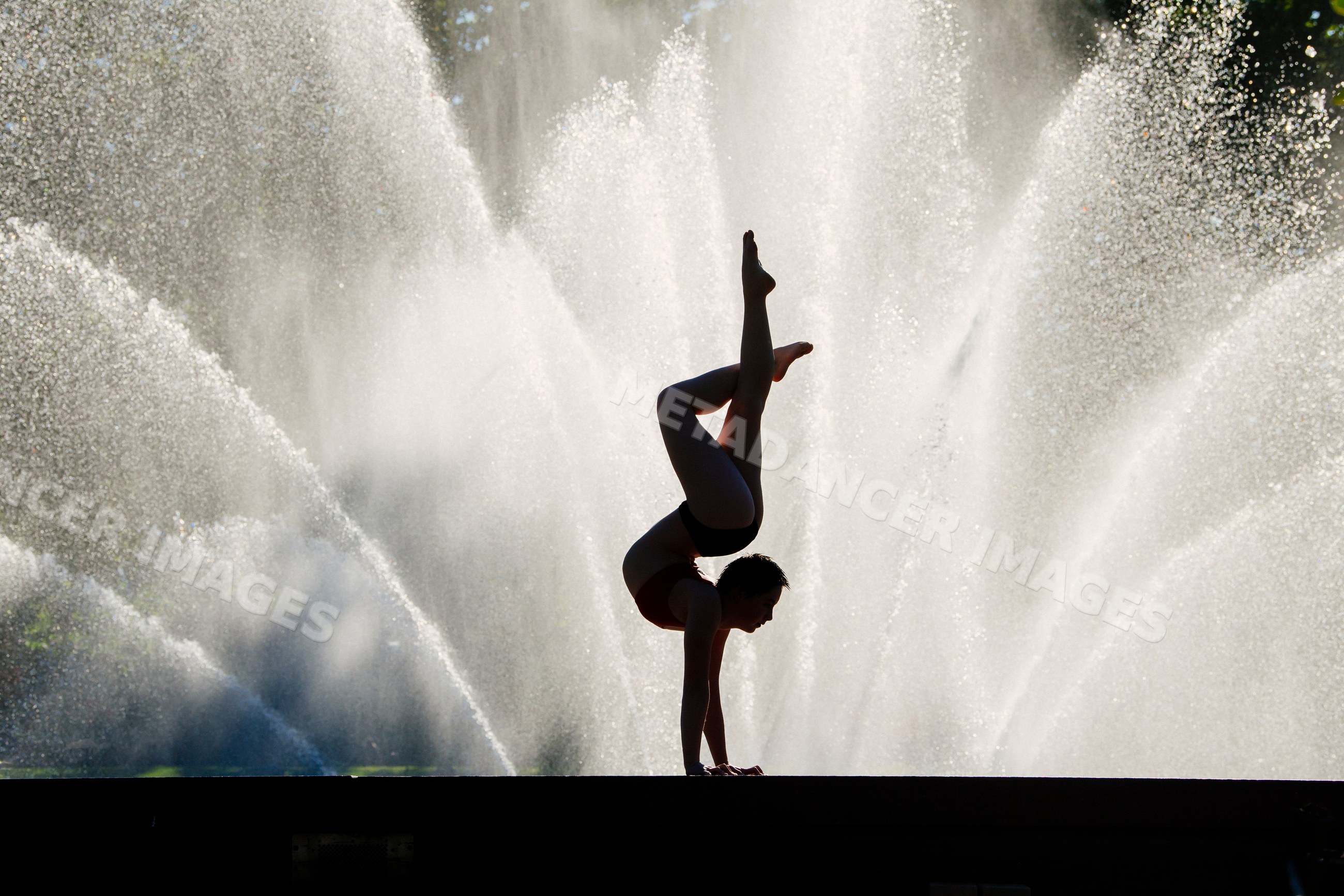 Female gymnast performing handspring silhouette by water fountain