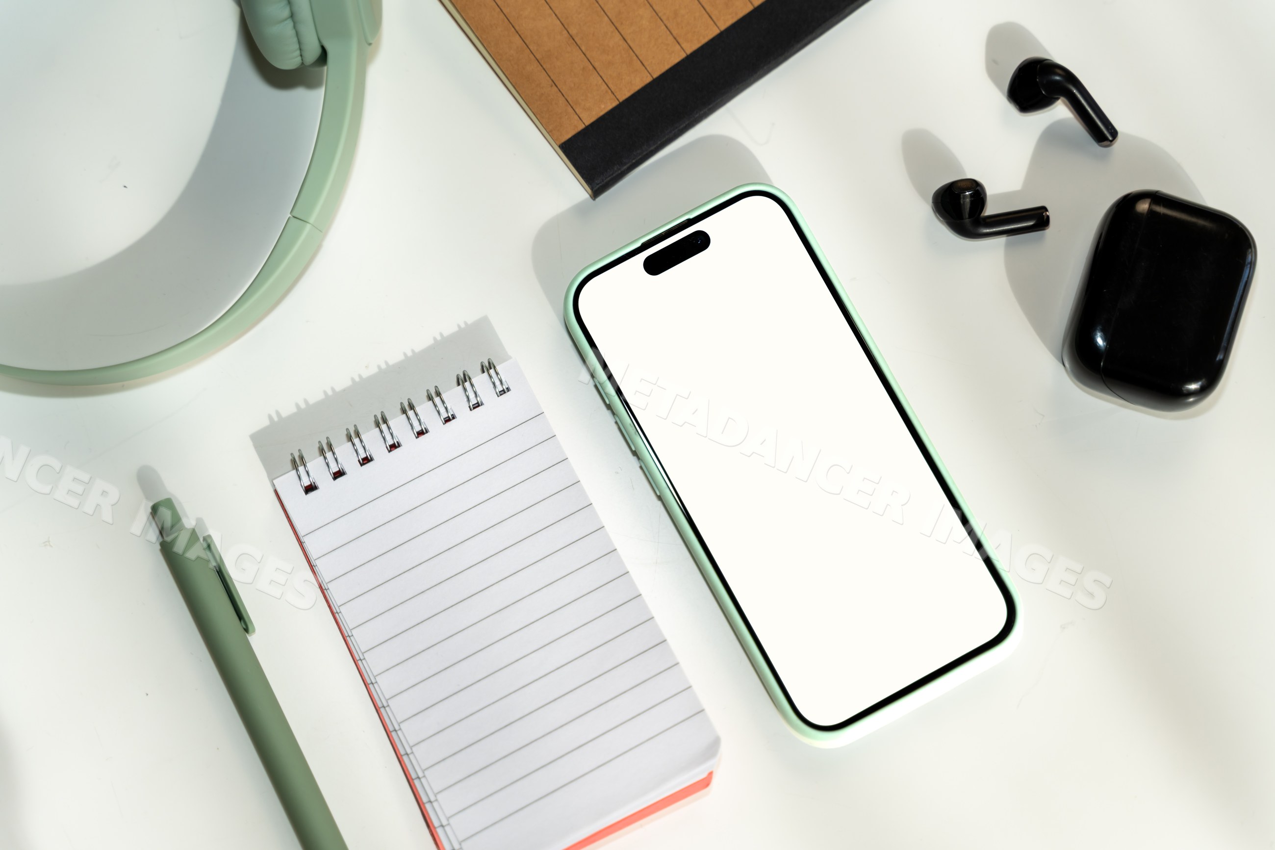 Smartphone and black wireless earbuds on white desk with notepad, pen