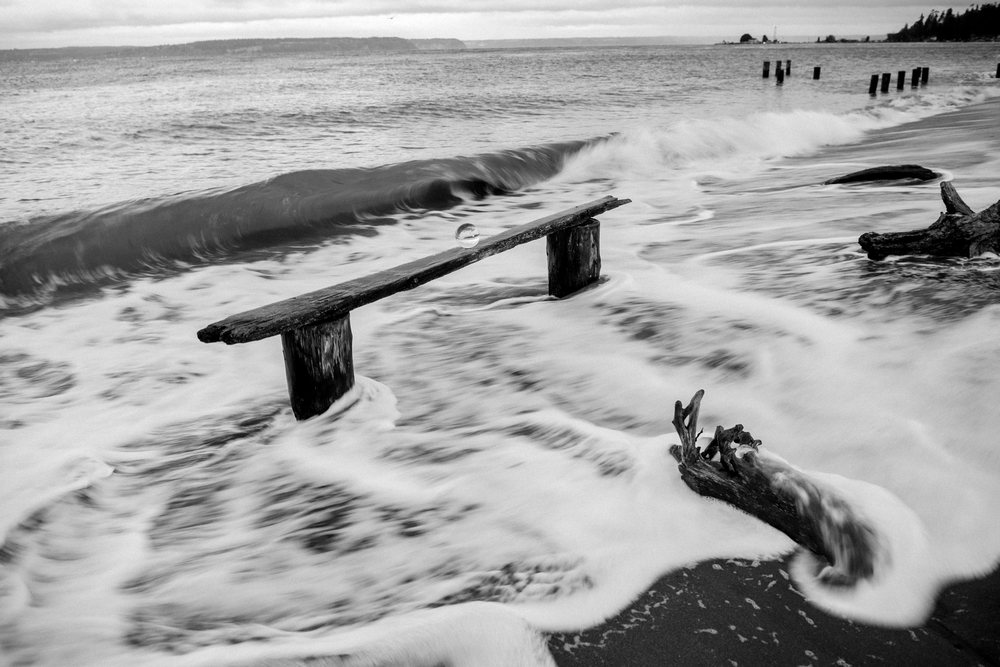 Waves crashing over driftwood and wooden beam