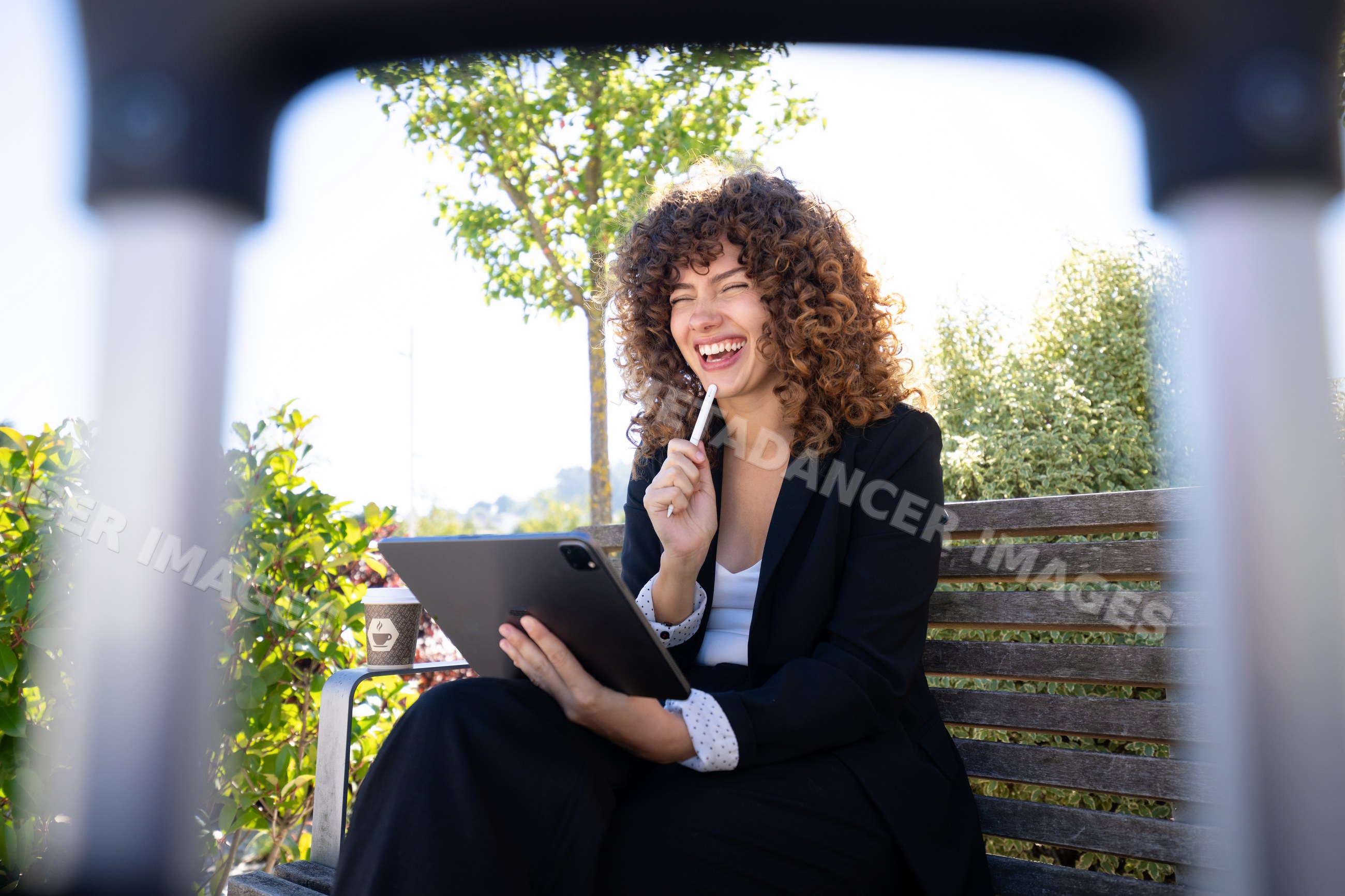 White woman laughing with tablet on bench outdoors