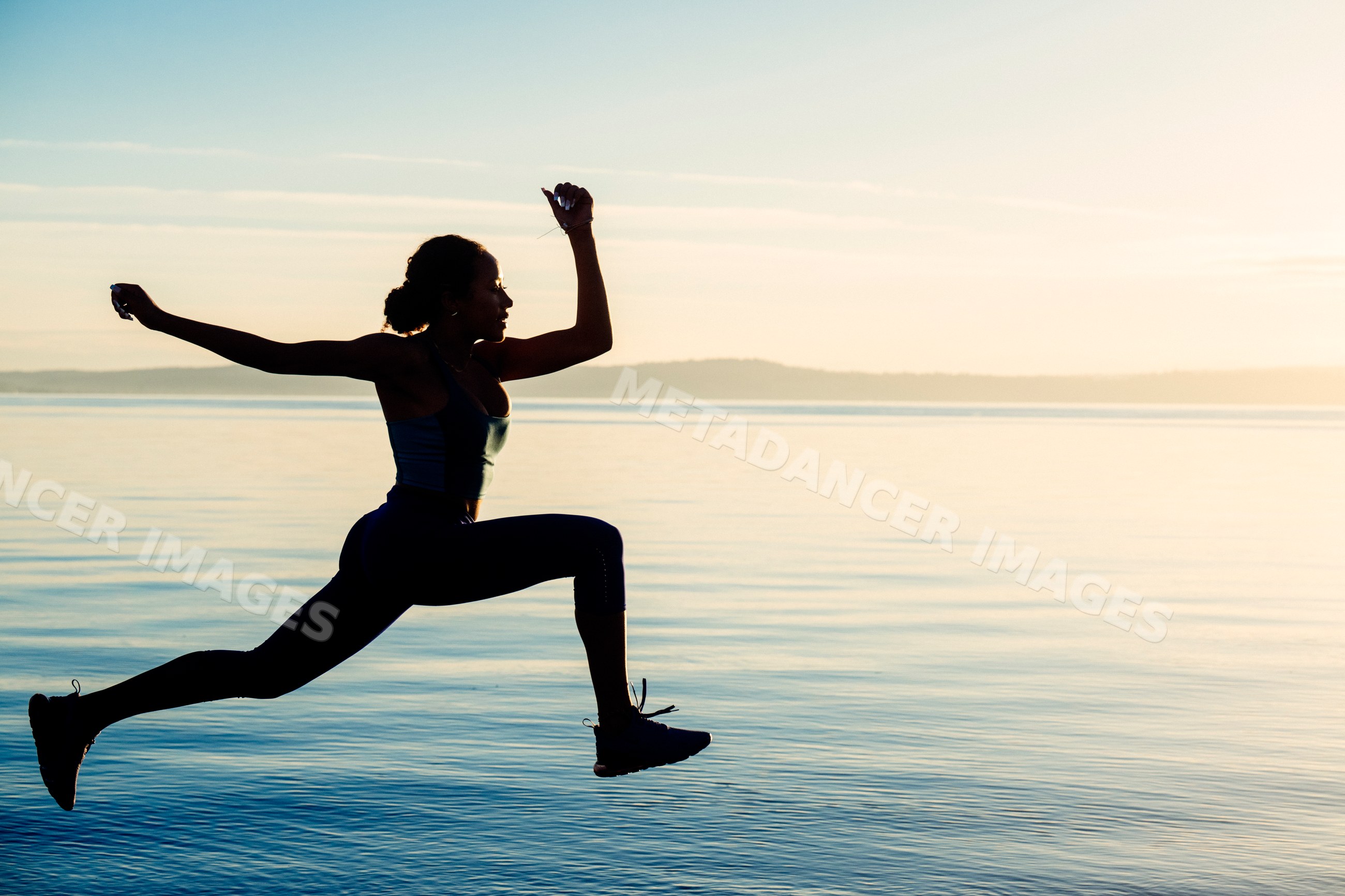 Hispanic woman jumping in silhouette outdoor exercise pose by lake