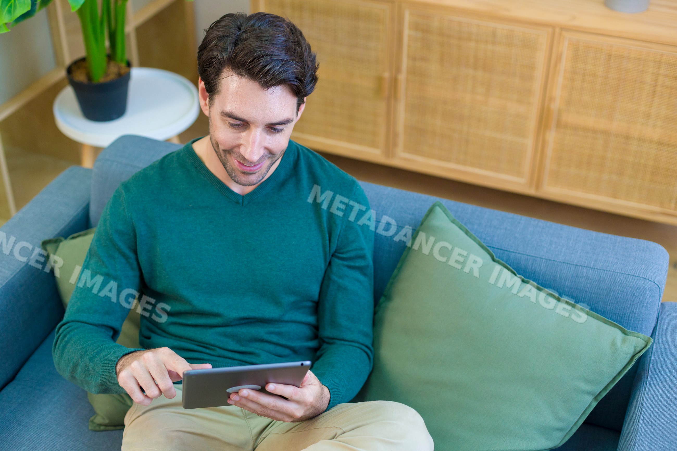 Young white man sitting on couch using tablet in modern home
