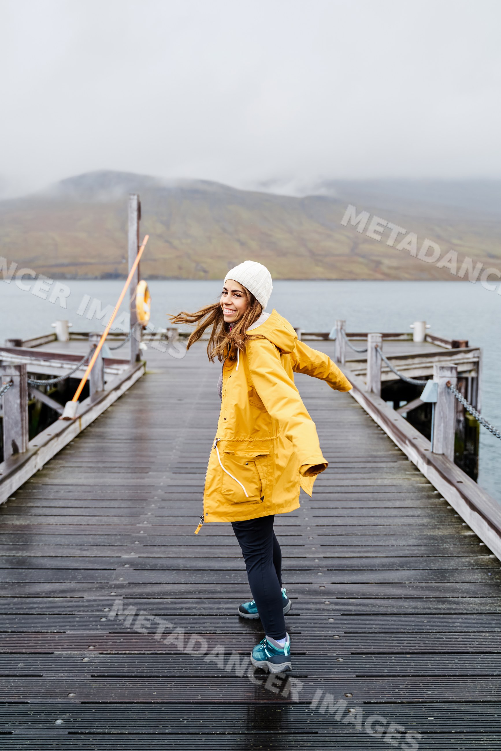 A white woman in a yellow rain jacket enjoys walking on a wooden pier