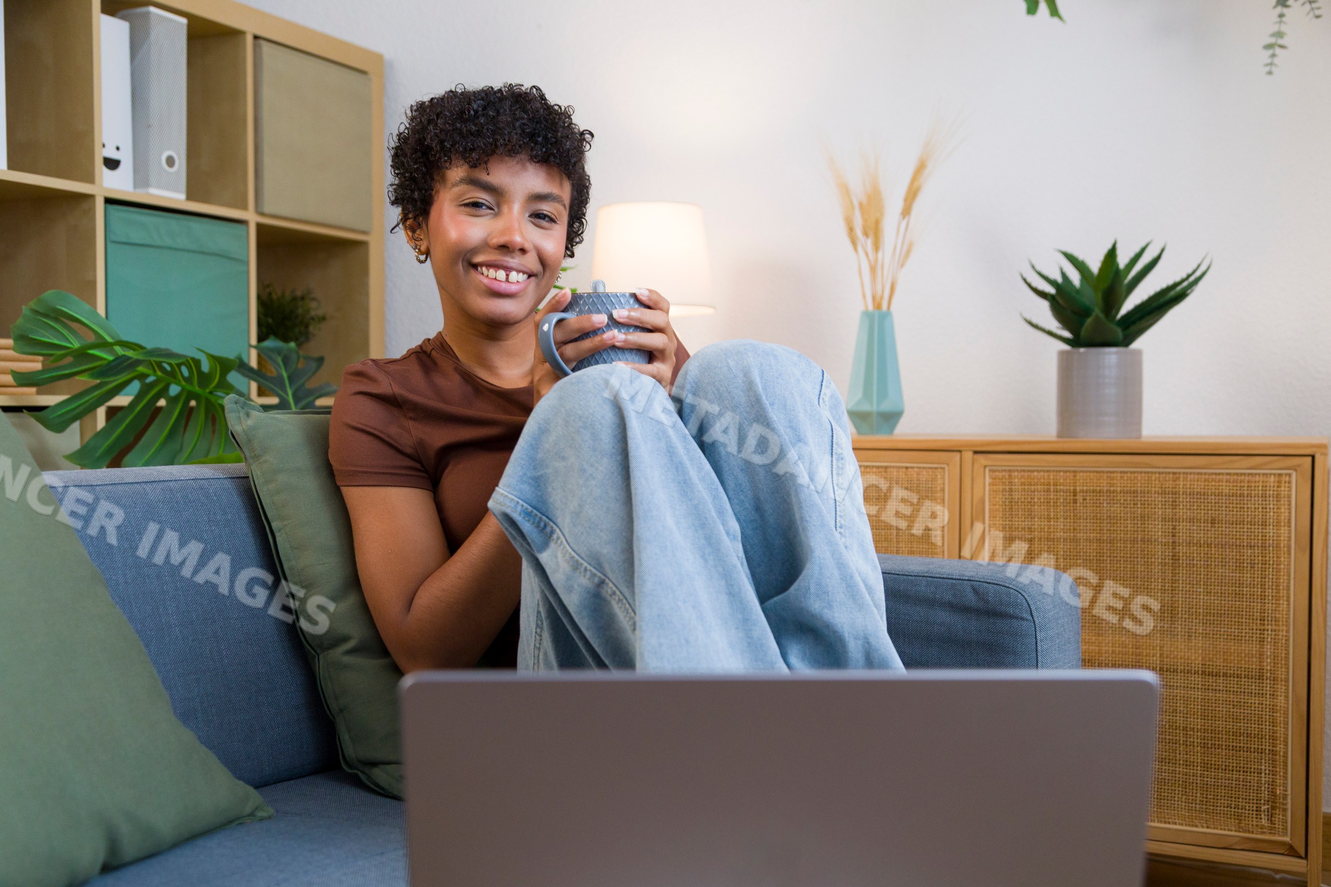 African American woman holding mug sitting on sofa in home living room