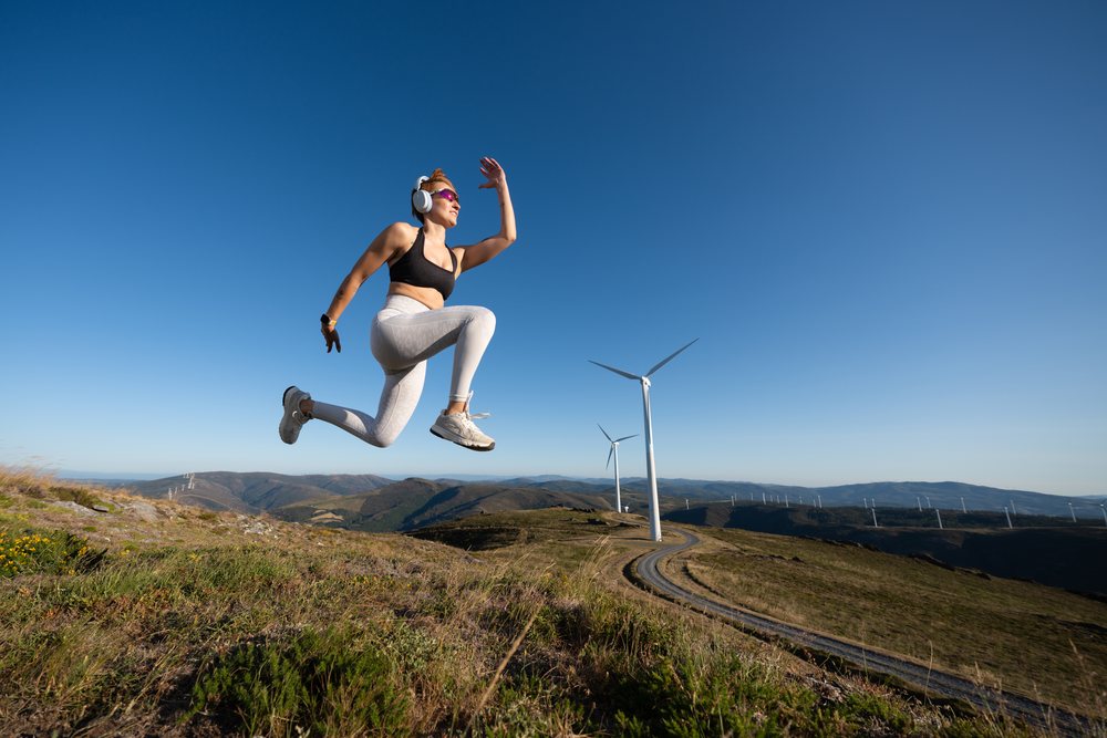 A young white woman jumps energetically on a mountain trail with wind