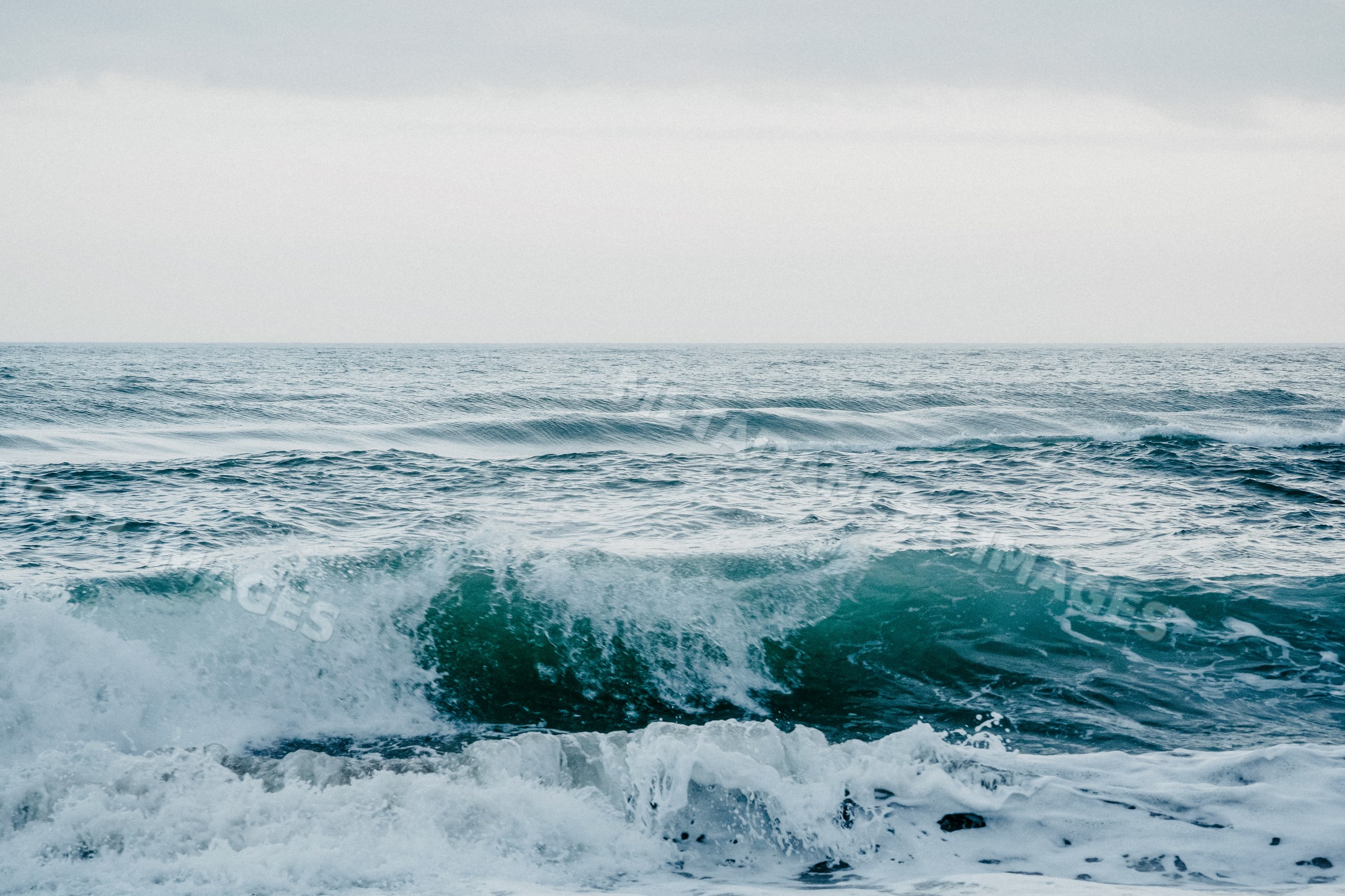 Ocean waves breaking and rolling under cloudy sky