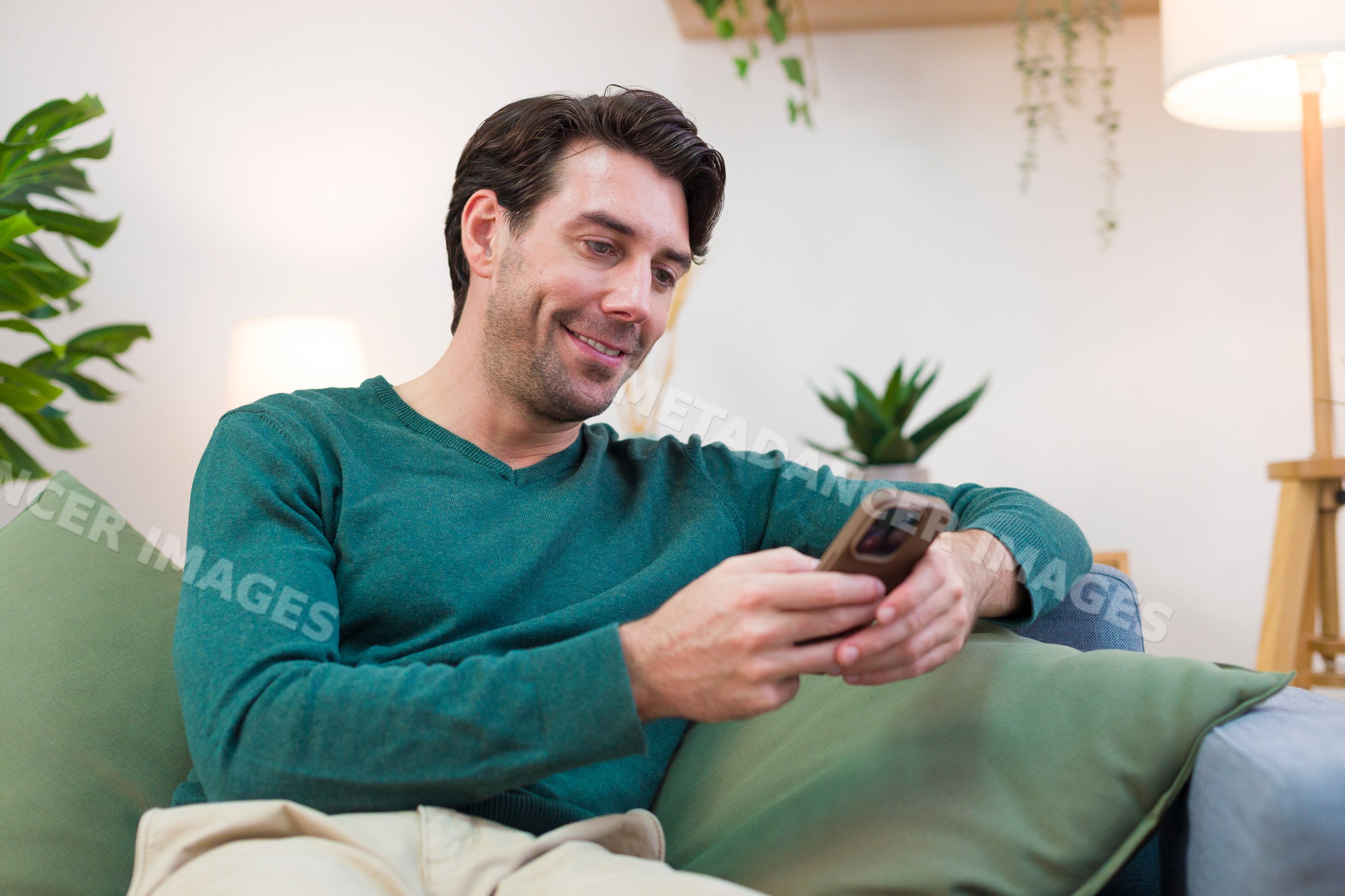 White man sitting on couch using smartphone at home