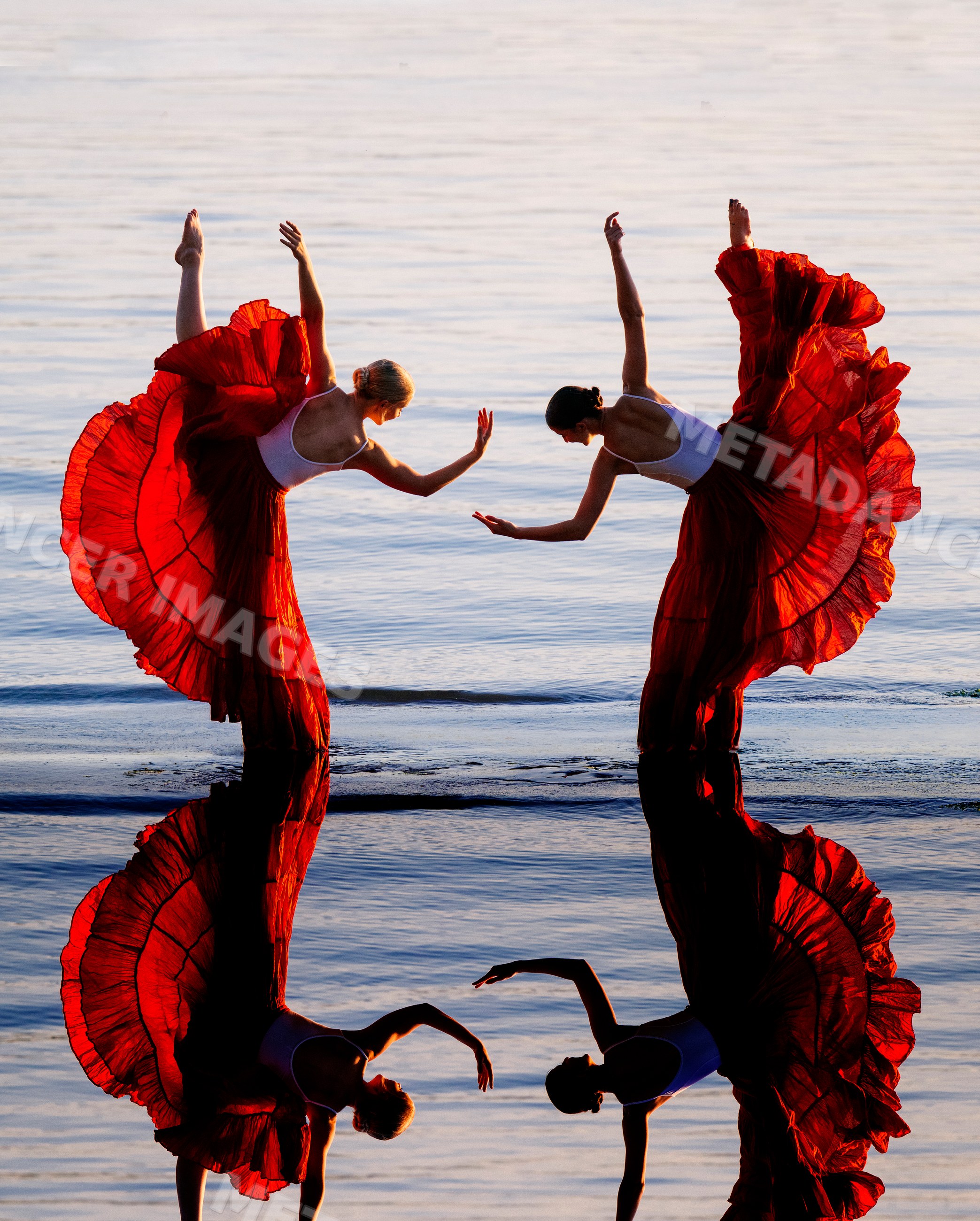 Two white women practicing partner yoga acrobatics with red skirts