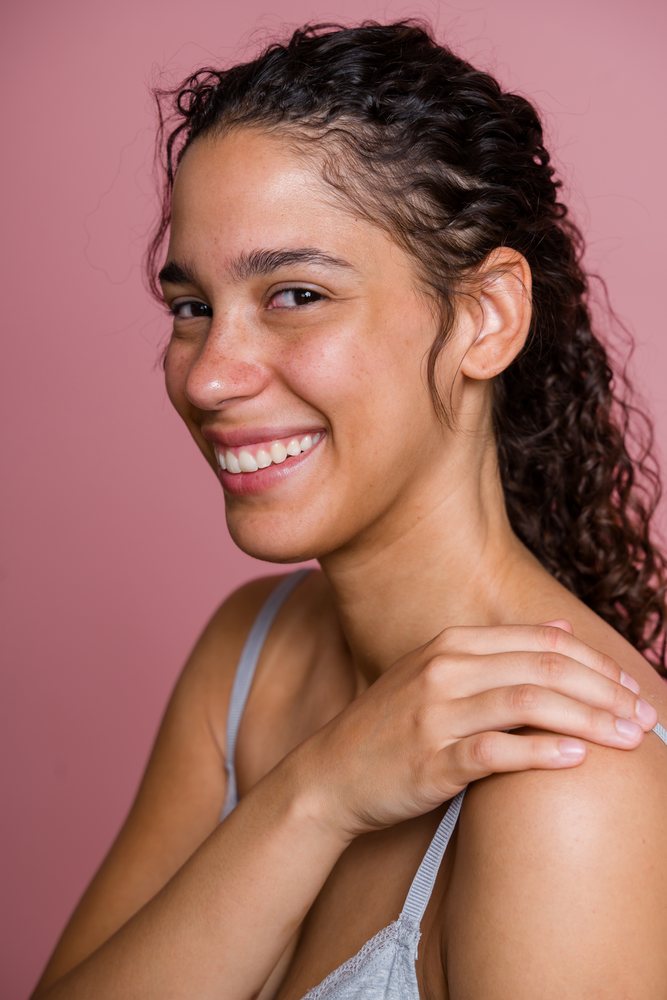 Hispanic woman smiling in profile with hand on shoulder against pink