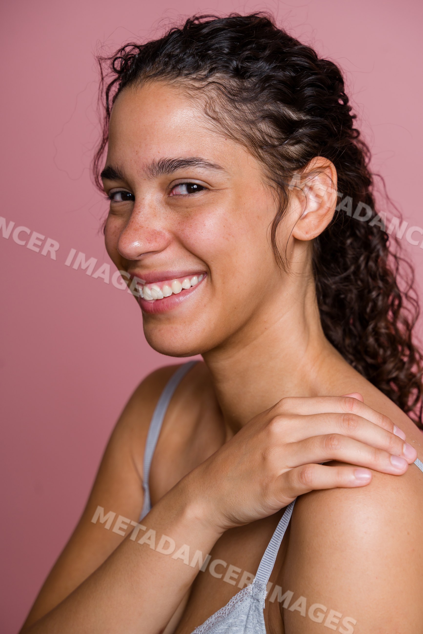 Hispanic woman smiling in profile with hand on shoulder against pink