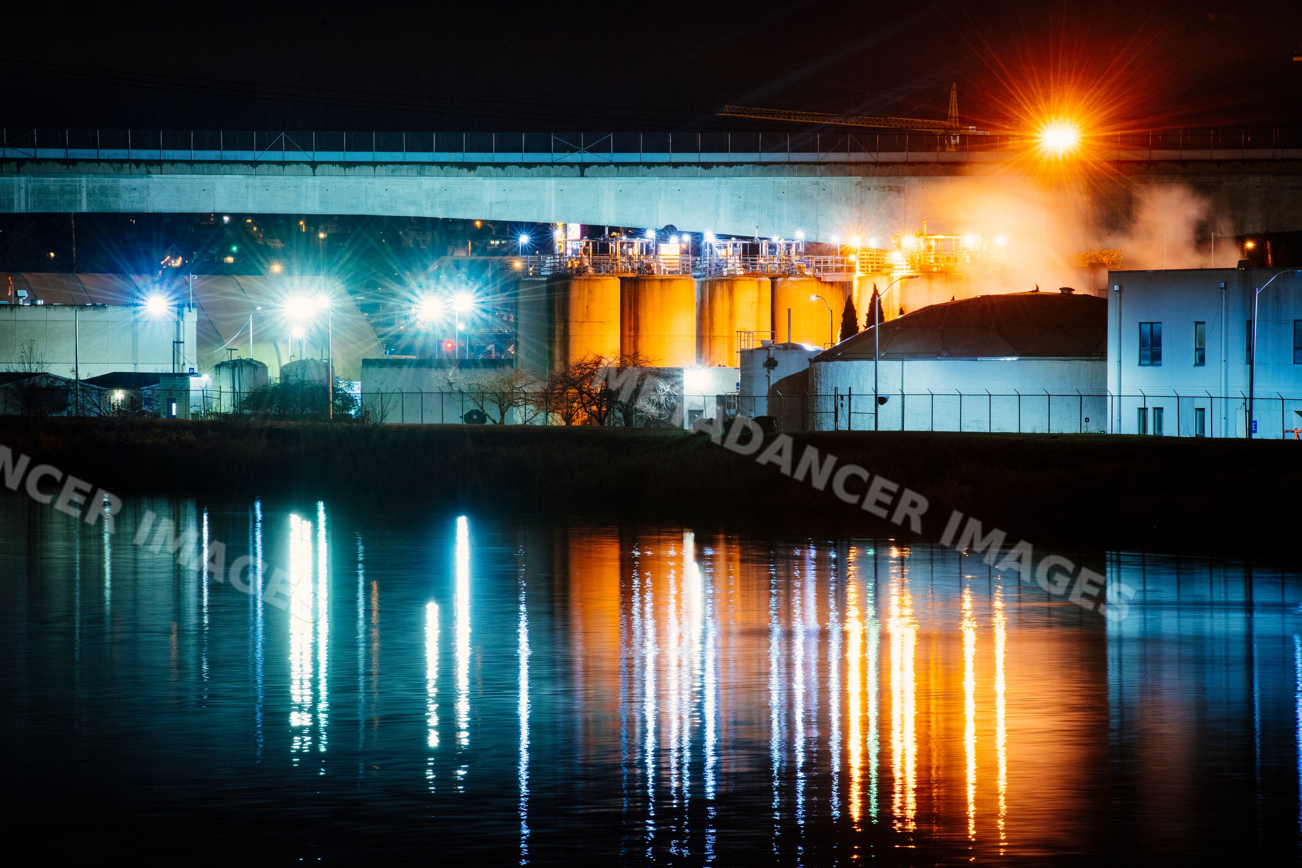 Industrial plant with illuminated storage tanks and water reflection