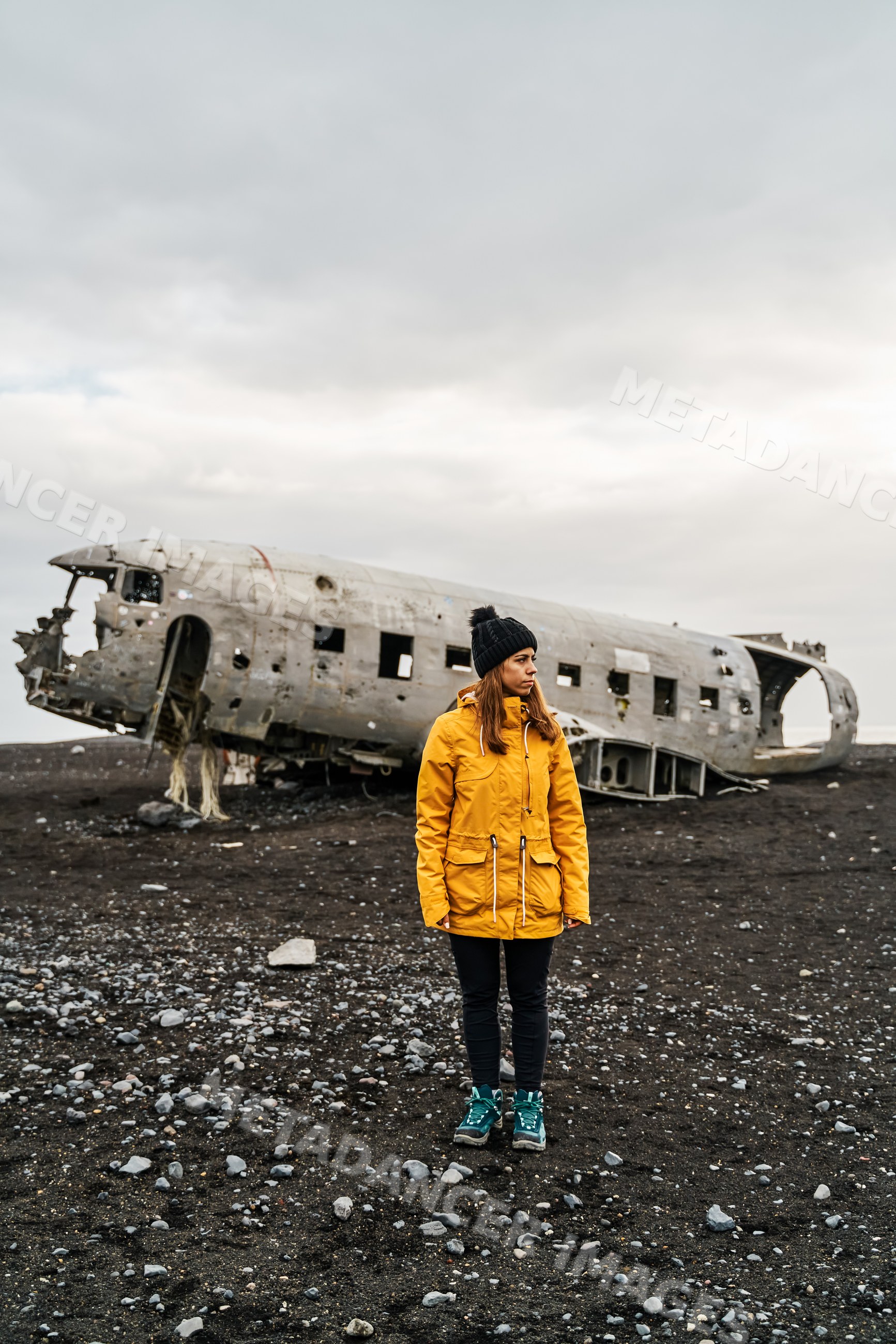 A white woman stands by a crashed airplane wreck on volcanic terrain