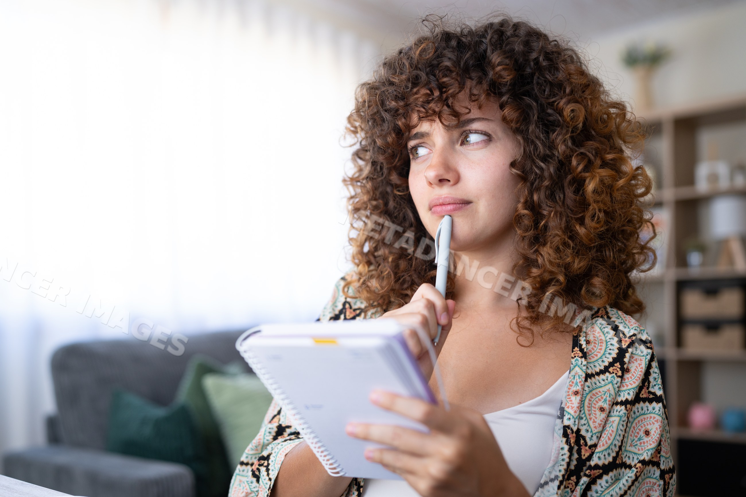 White girl thoughtfully holding pen and notebook at home in Spain