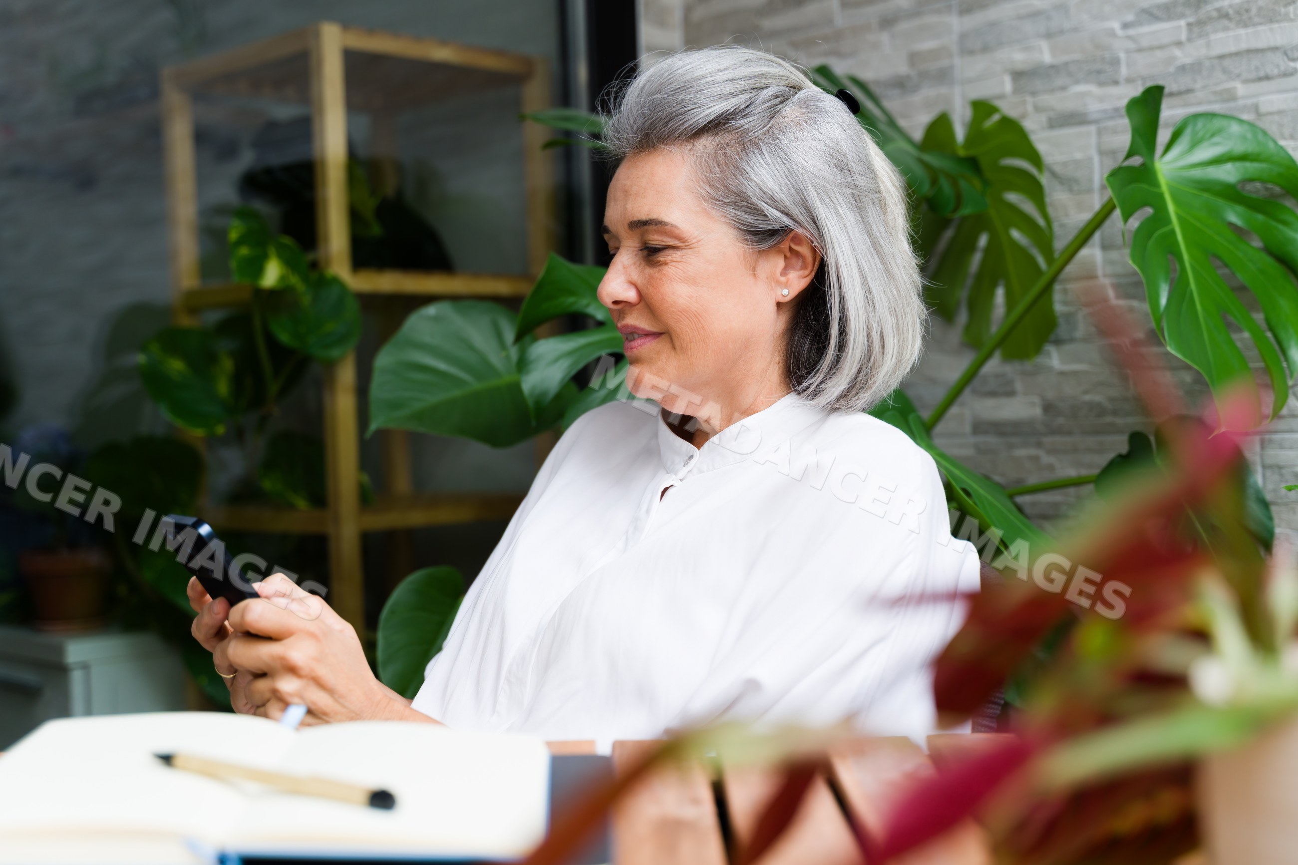 White Woman with gray hair using a smartphone among houseplants