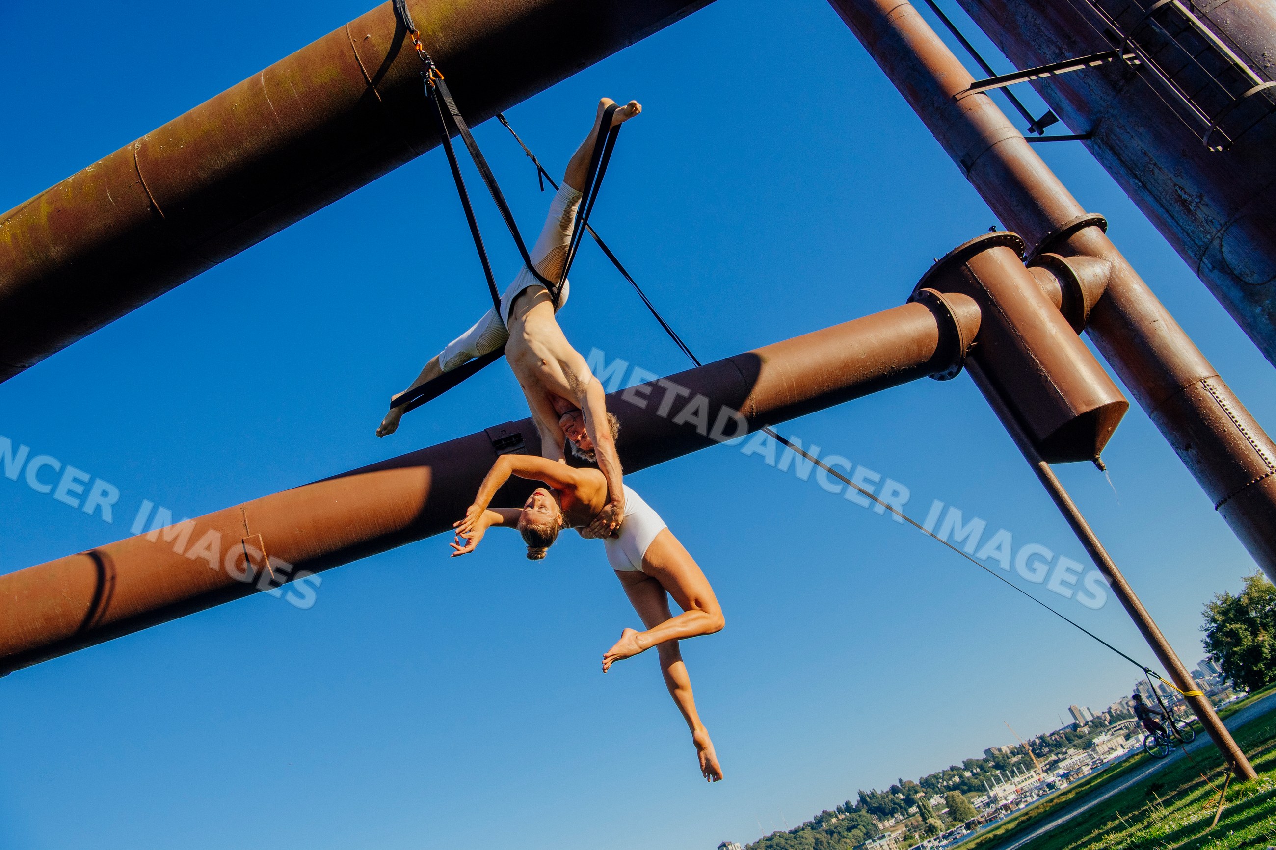 Aerial acrobats perform outdoor routine on industrial pipes in a park
