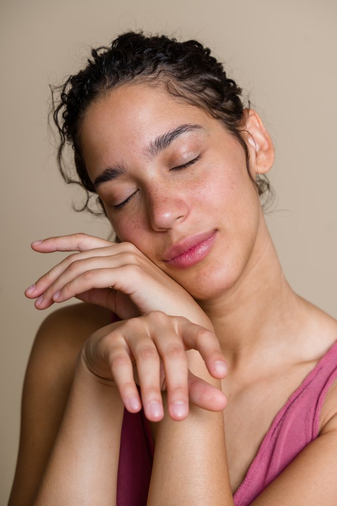 Hispanic woman with closed eyes resting face on hands in calm pose