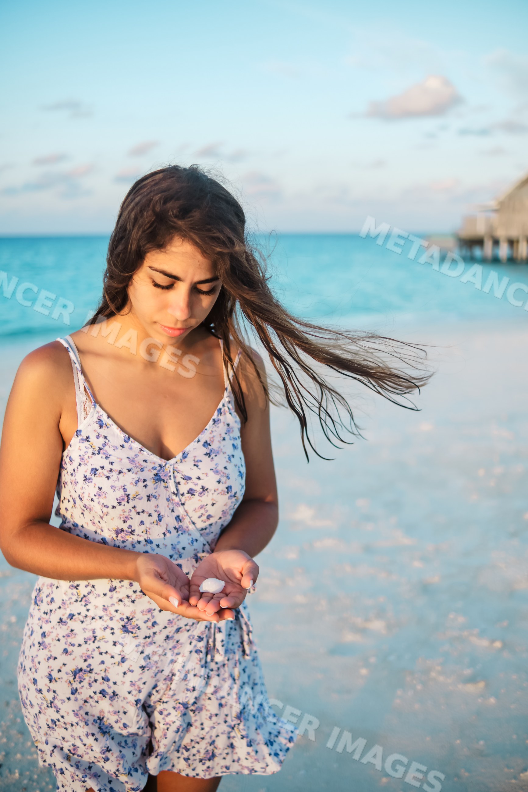 A young white woman holds a seashell on a beach in a beach