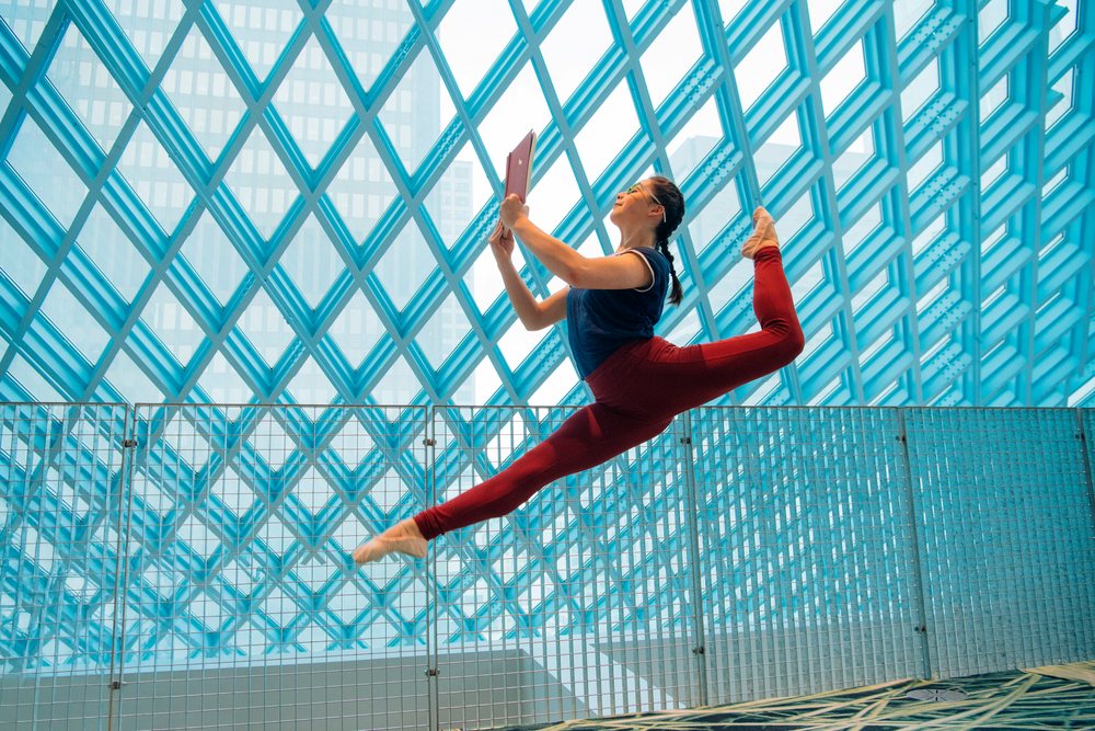 Woman performing ballet leap while reading a book in a library