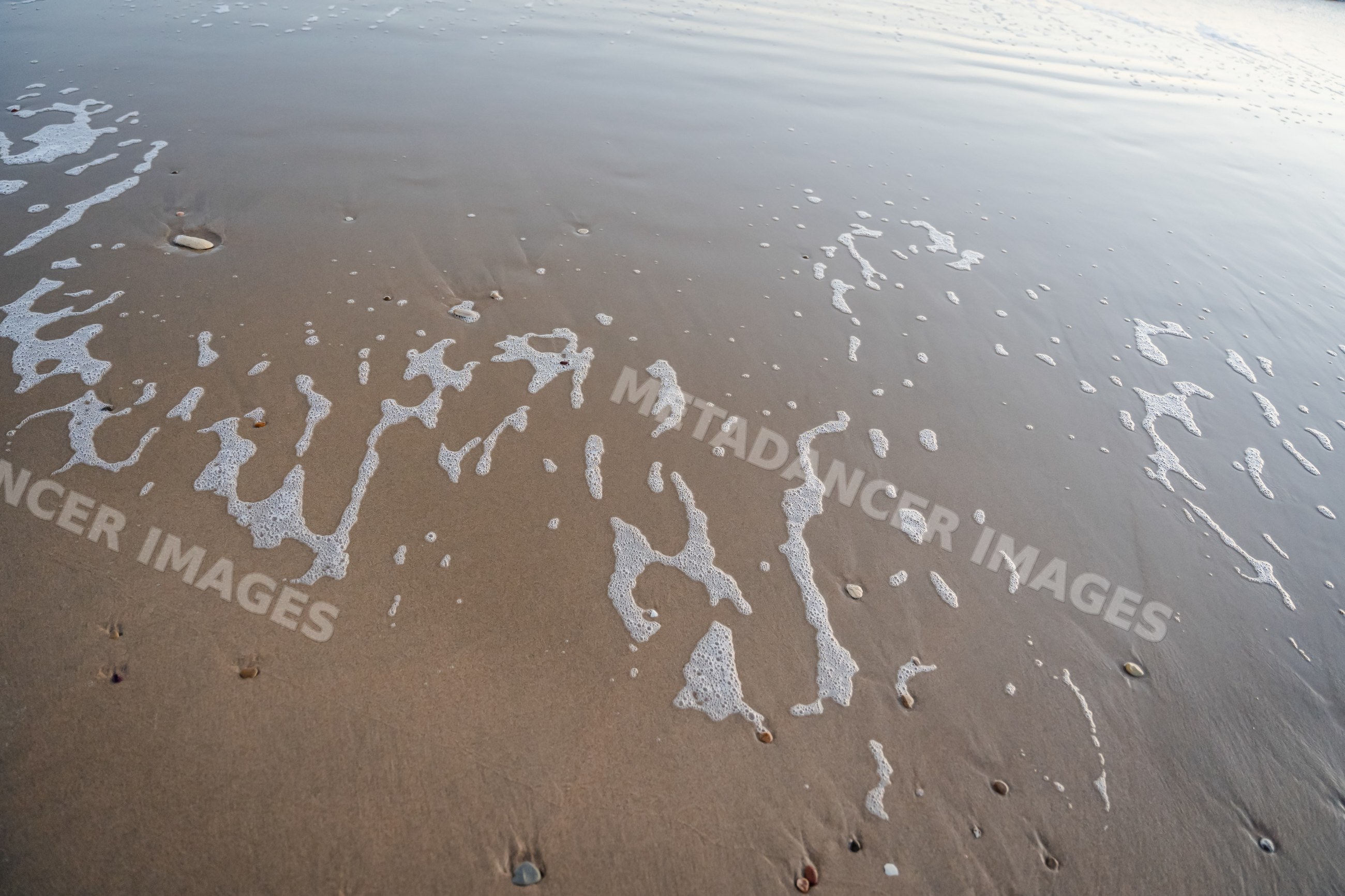 Sea foam and wet sand along spanish beach shoreline