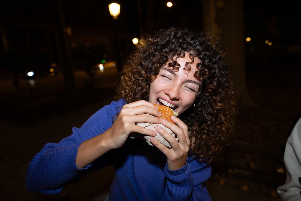 White woman eating a burger outdoors at night