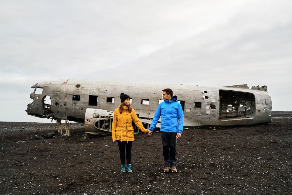 Couple holding hands near a crashed airplane wreck on Iceland's black