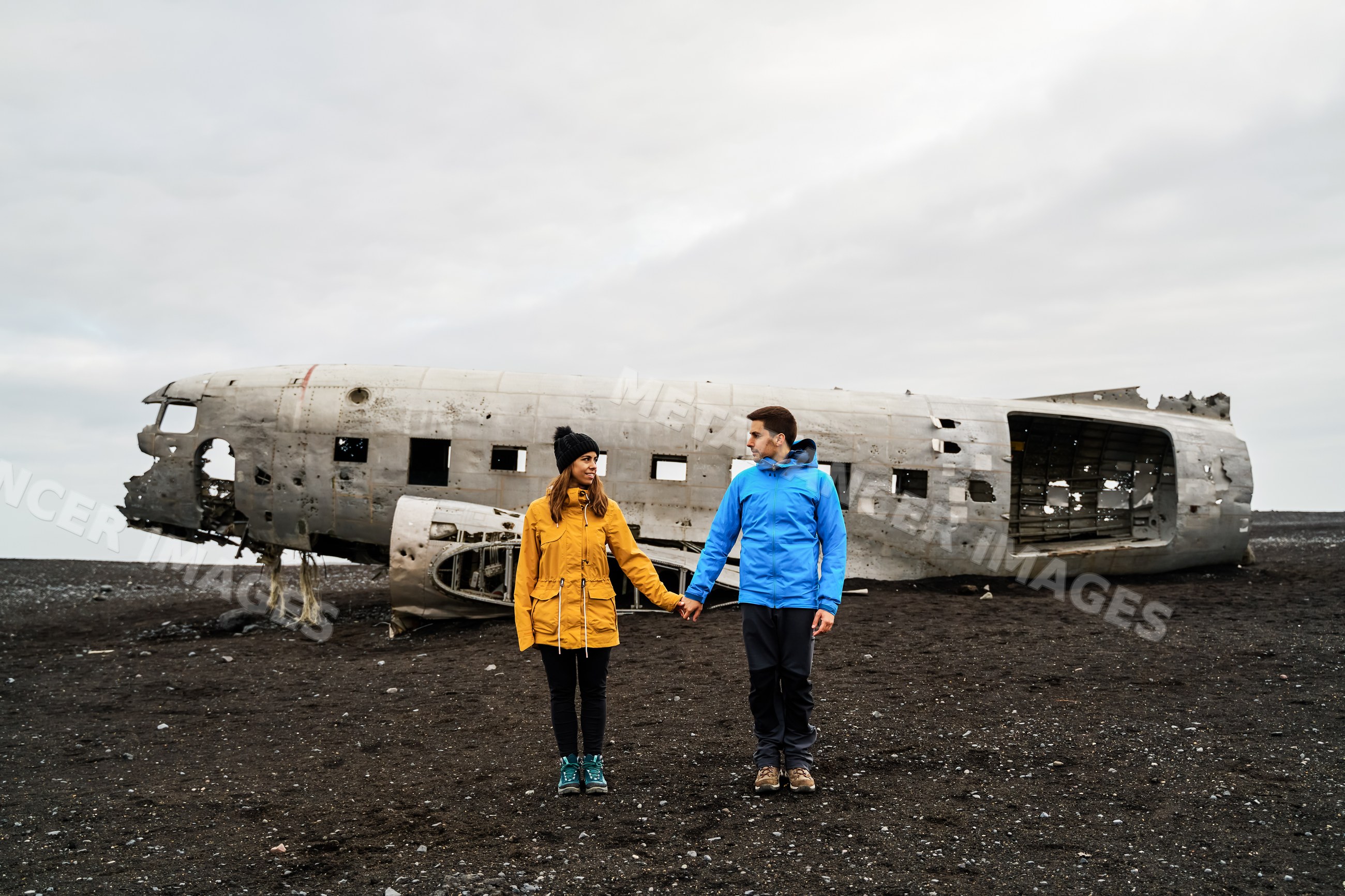 Couple holding hands near a crashed airplane wreck on Iceland's black