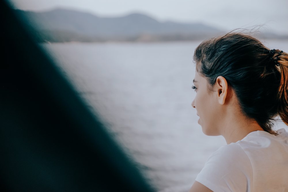 White woman gazing at the sea from boat with mountain landscape