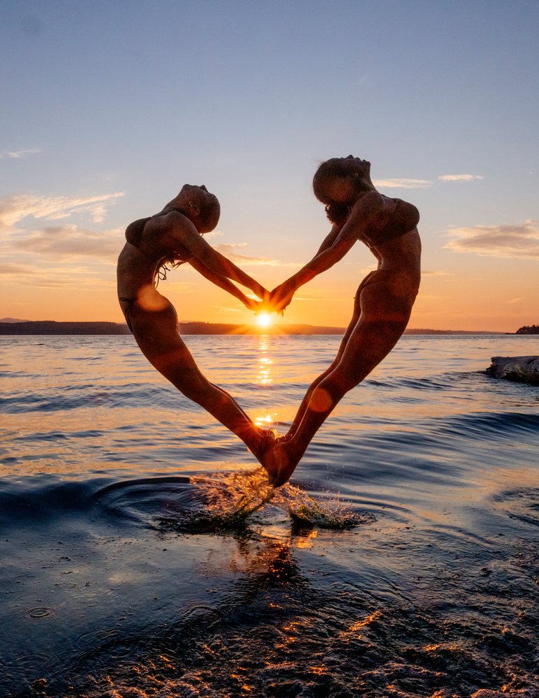Two people doing partner acrobatics yoga jumping at sunset over water