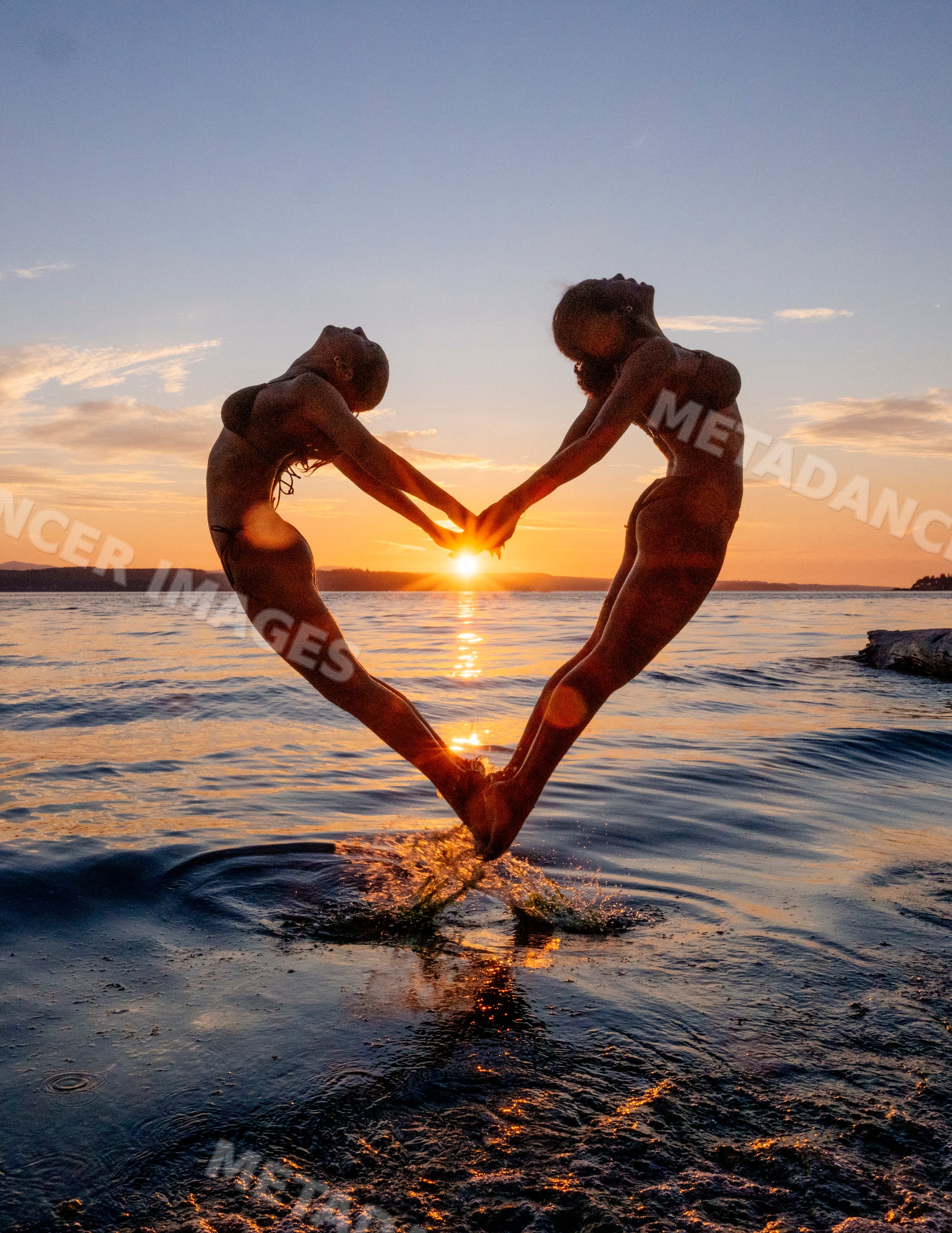Two people doing partner acrobatics yoga jumping at sunset over water