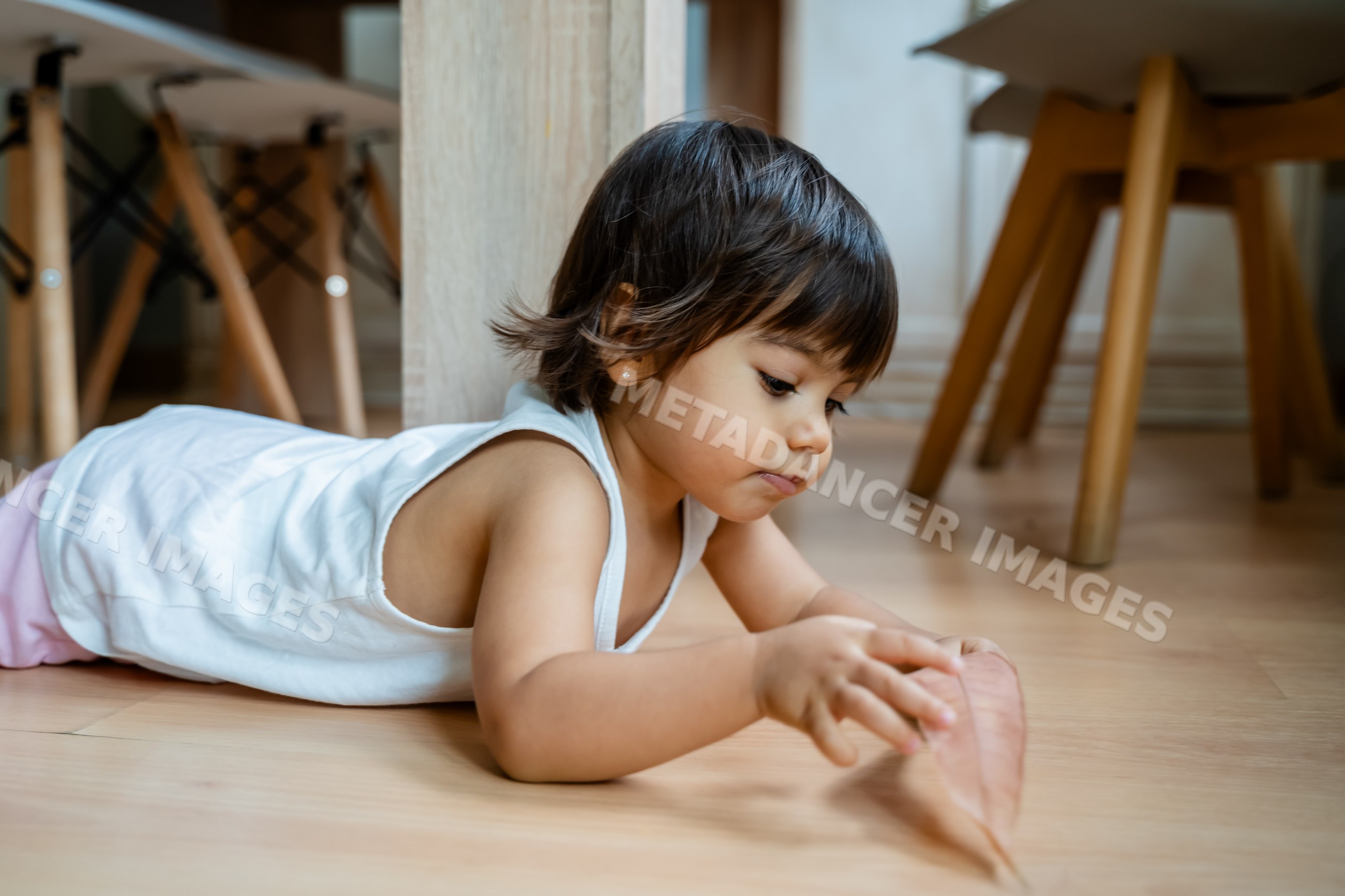 Toddler white child playing with dried leaf on wooden floor indoors