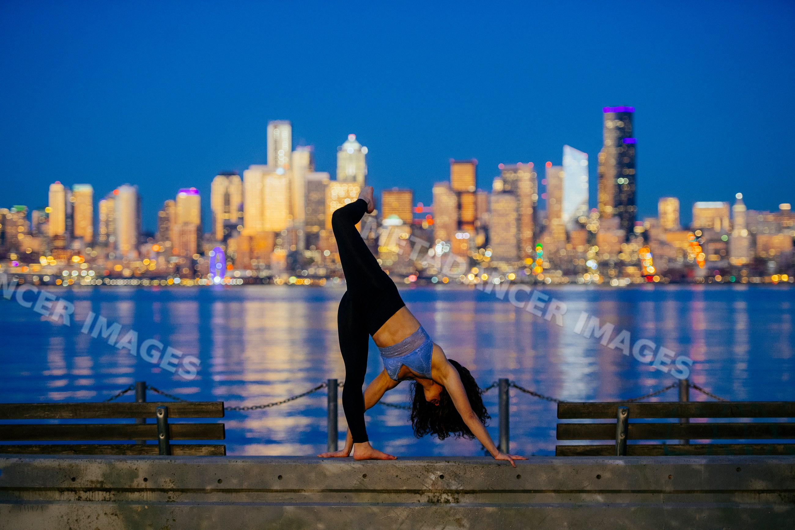 White woman practicing yoga backbend by Seattle waterfront at dusk